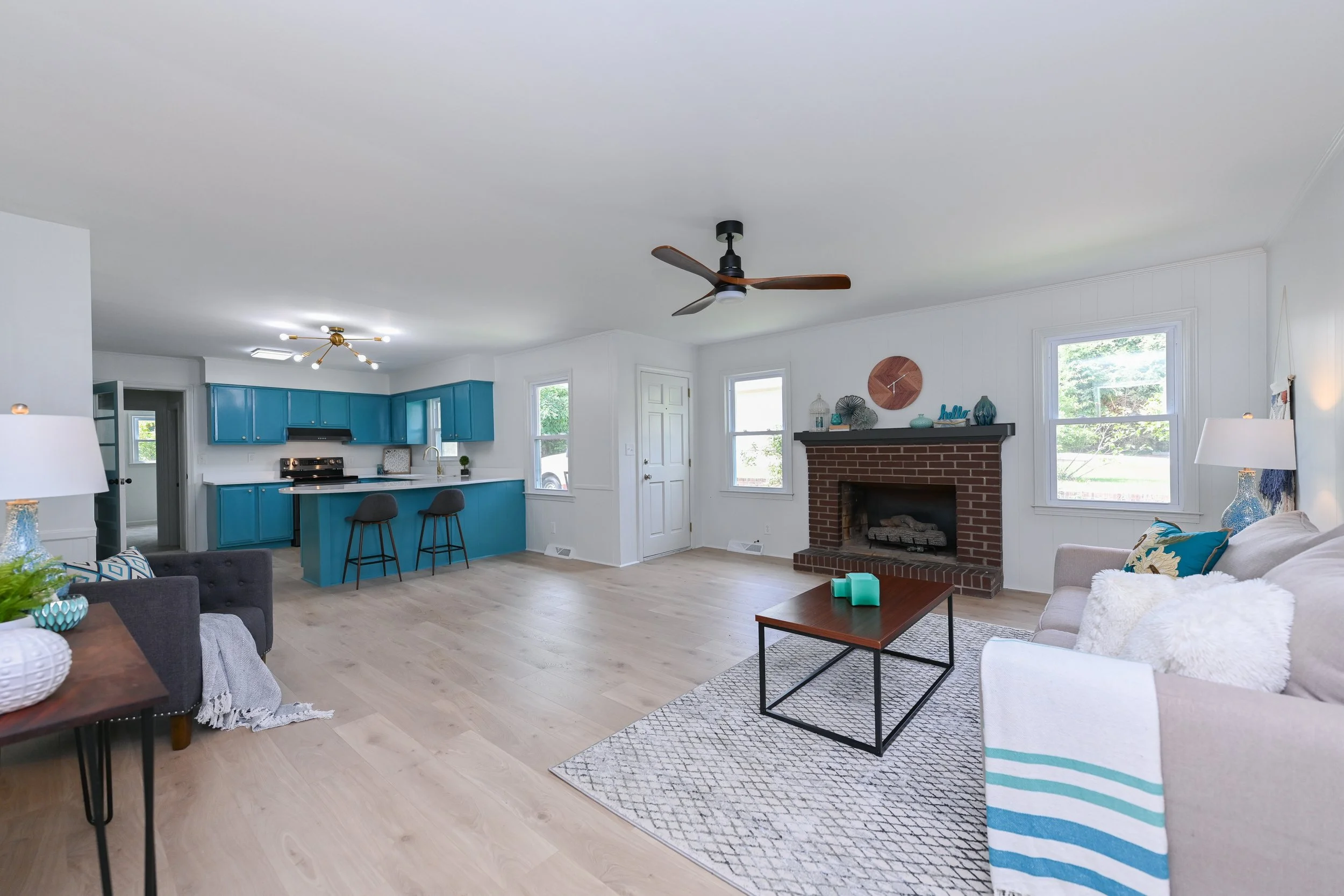 Renovated open-plan living area at 33 Oriole Street in Greenville, SC, featuring a brick fireplace, vibrant blue kitchen cabinetry, breakfast bar, light wood flooring, and contemporary finishes.