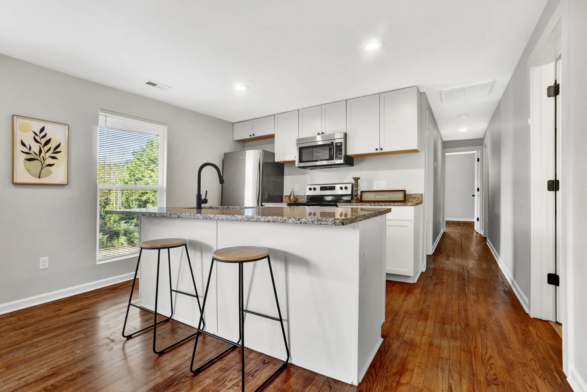 Renovated kitchen at 1317 Hub Wilson Road in Landrum, SC, featuring white cabinetry, granite countertops, stainless steel appliances, a breakfast bar with seating, and hardwood floors.