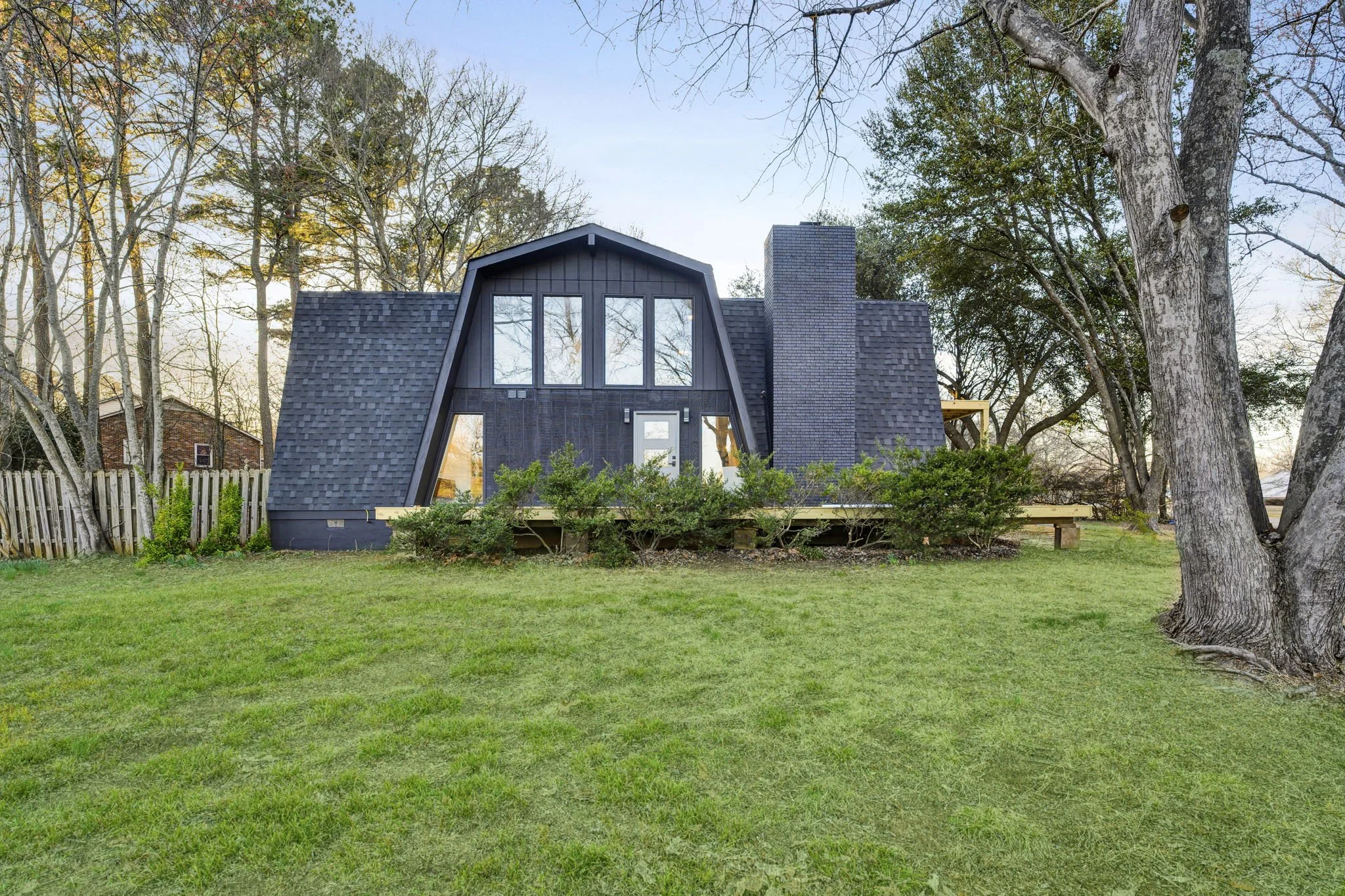 Renovated contemporary home at 112 Wayland Drive in Duncan, SC, featuring a distinctive gambrel-style roof, dark exterior siding, large windows, a brick chimney, and mature landscaping.