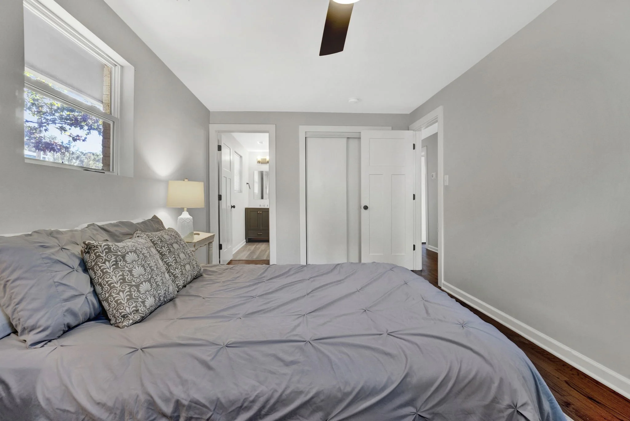 Renovated bedroom at 1317 Hub Wilson Road in Landrum, SC, featuring hardwood floors, soft gray walls, a ceiling fan, natural light, and access to an adjoining bathroom.