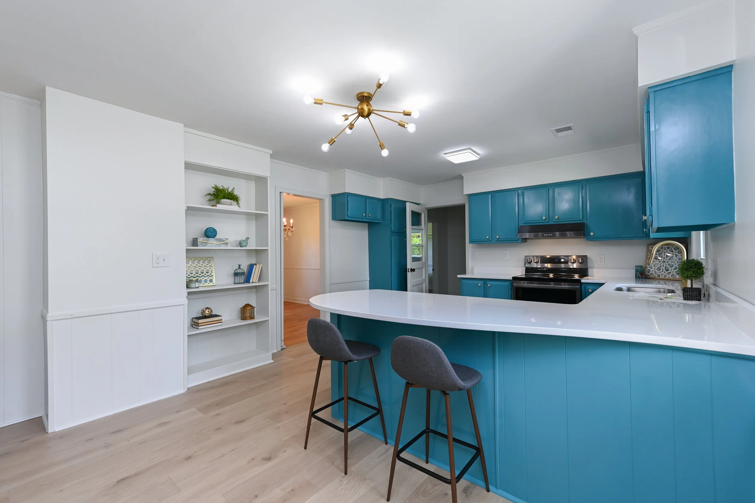 Renovated kitchen at 33 Oriole Street in Greenville, SC, featuring vibrant blue cabinetry, white countertops, a spacious breakfast bar, built-in shelving, and modern brass lighting.