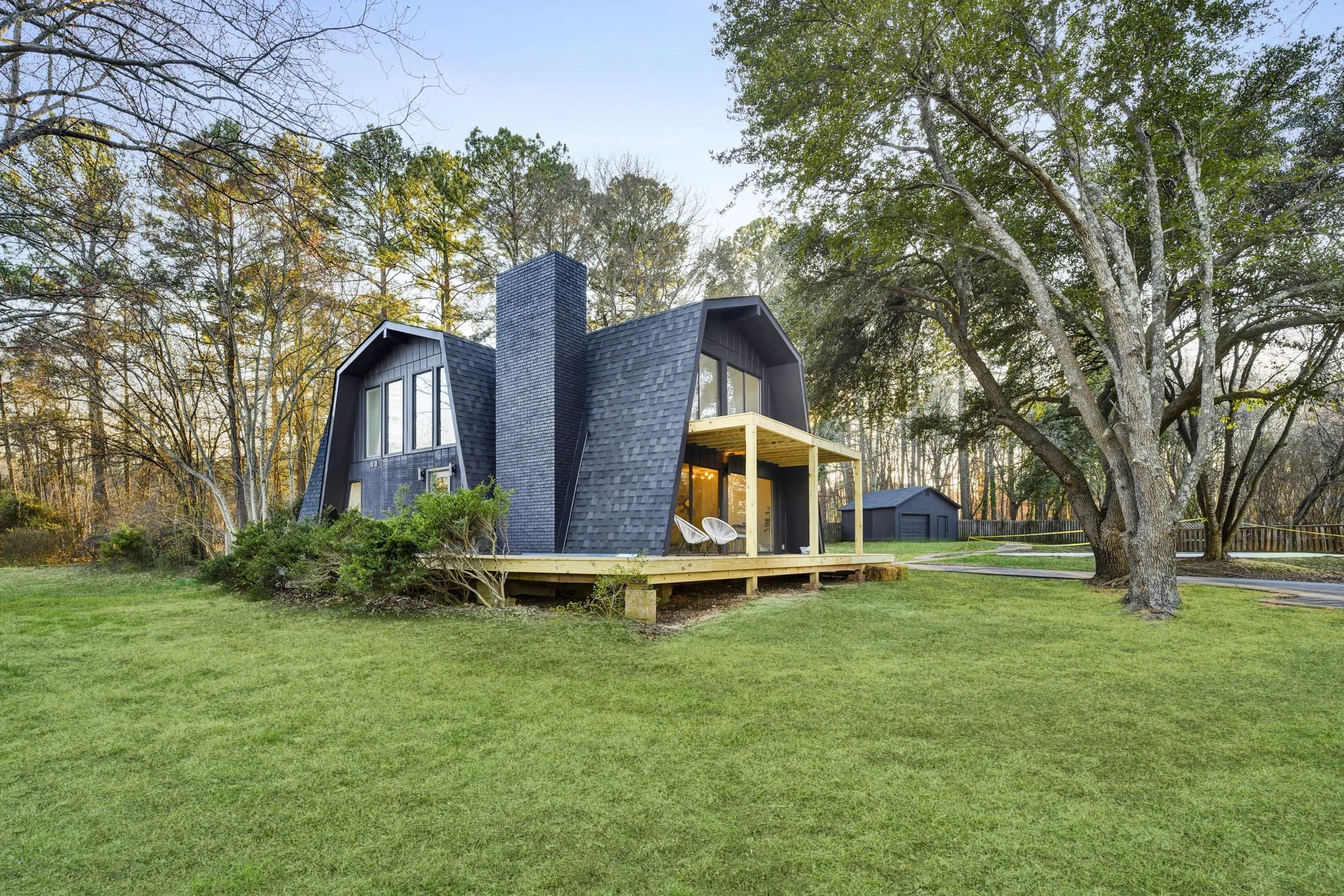 Renovated residential property at 112 Wayland in Greenville, SC, featuring a distinctive dark gambrel-style roof, black exterior siding, natural wood porch, and spacious landscaped lawn surrounded by mature trees.