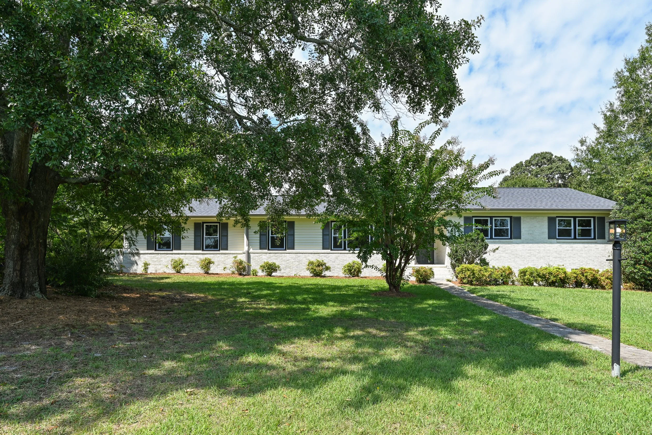 Renovated ranch-style home at 33 Oriole Street in Greenville, SC, featuring light-colored brick and siding, dark shutters, mature trees, and a spacious landscaped front lawn.