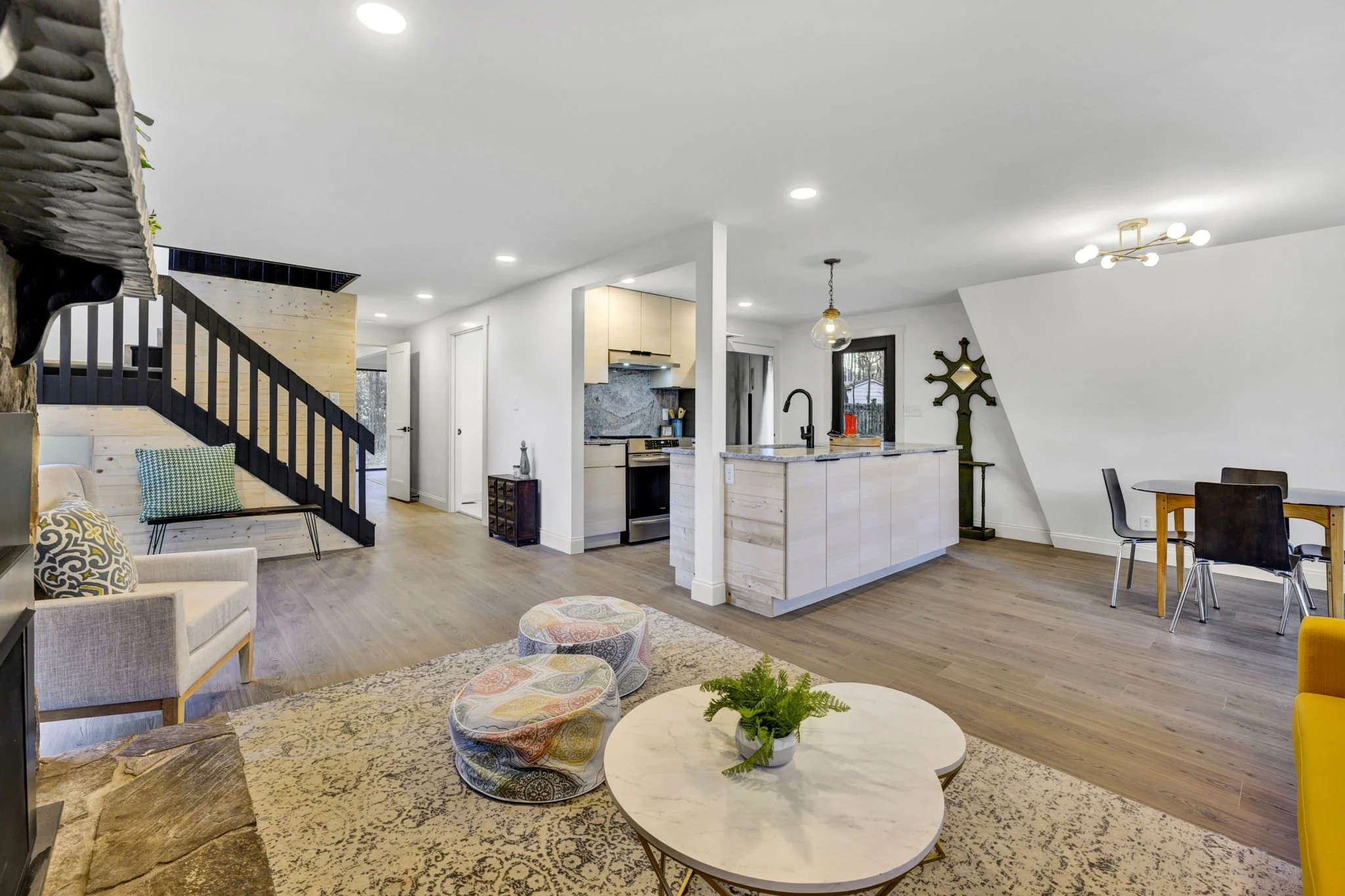Renovated open-plan living area at 112 Wayland Drive in Duncan, SC, featuring a modern kitchen with breakfast bar, light wood flooring, and a staircase with black railings and natural wood paneling.