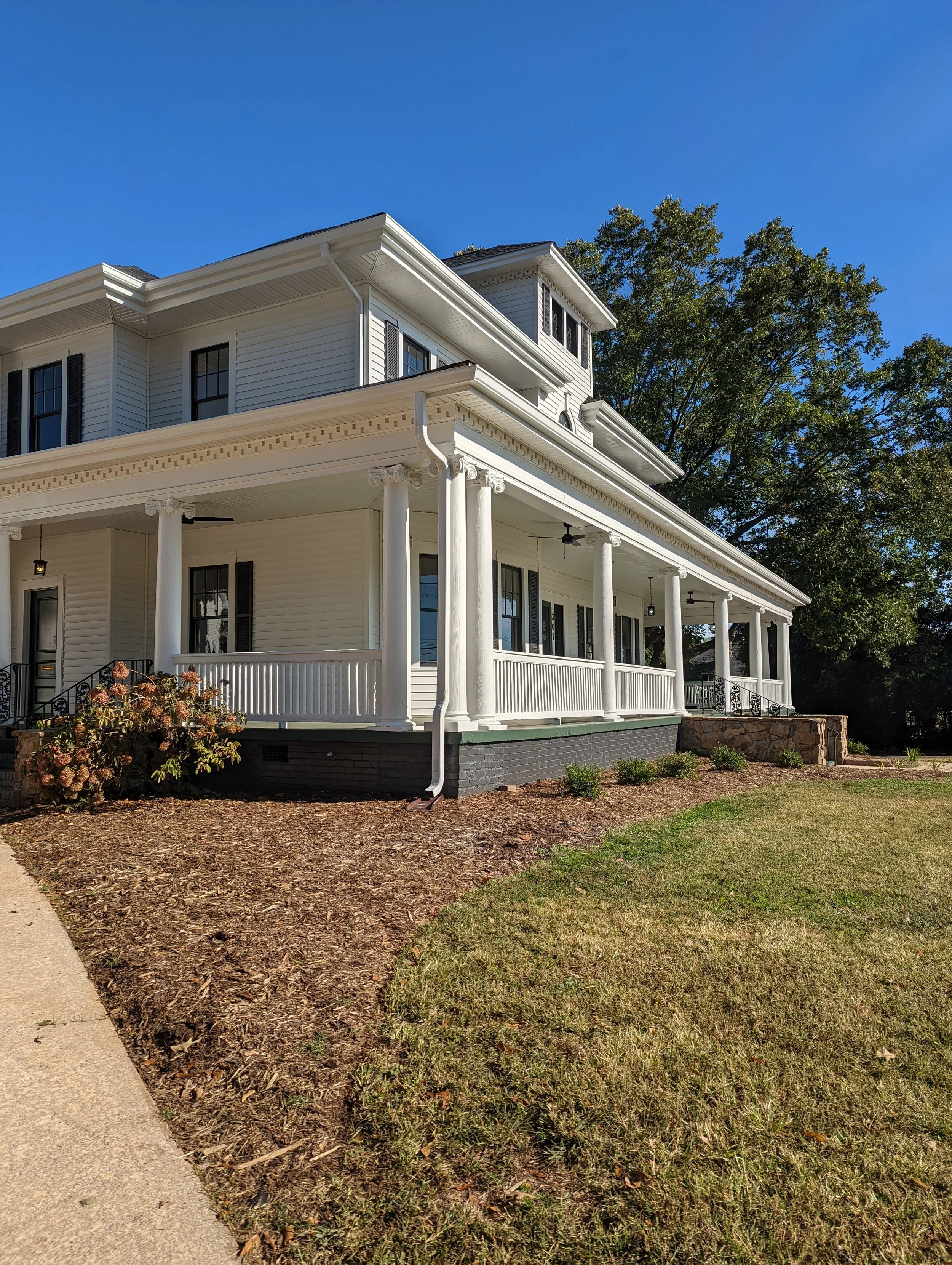 Restored exterior of Historic Hampton House 1908 in Pickens, SC, featuring white siding, black shutters, classical columns, and an expansive wraparound porch.