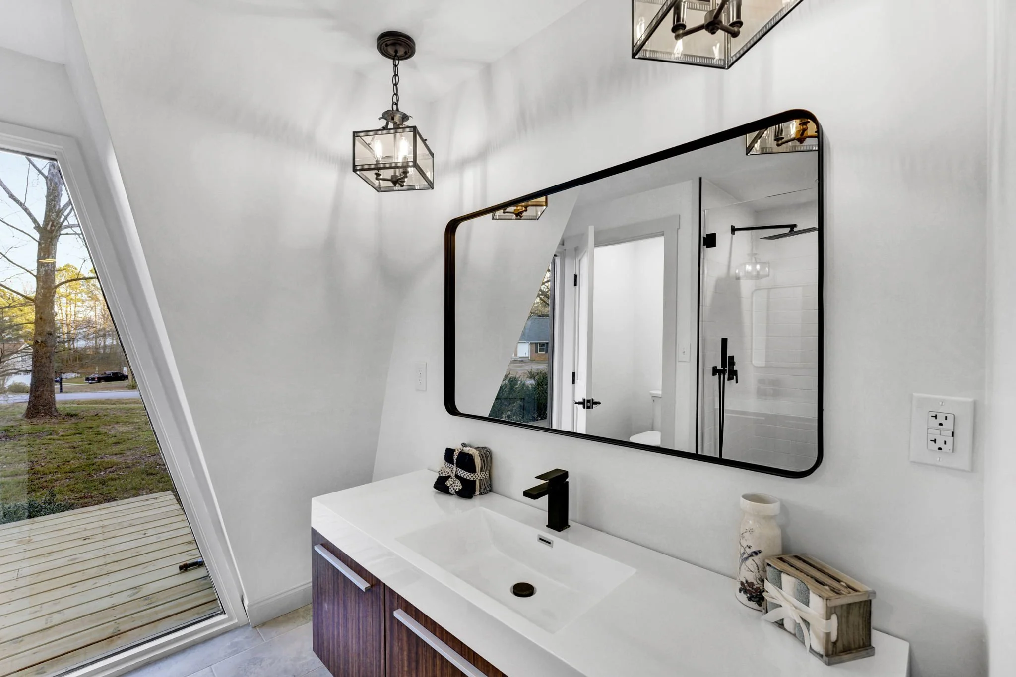 Modern bathroom at 112 Wayland Drive in Duncan, SC, featuring a wood vanity, white countertop, black fixtures, oversized mirror, and a distinctive angled window overlooking the yard.