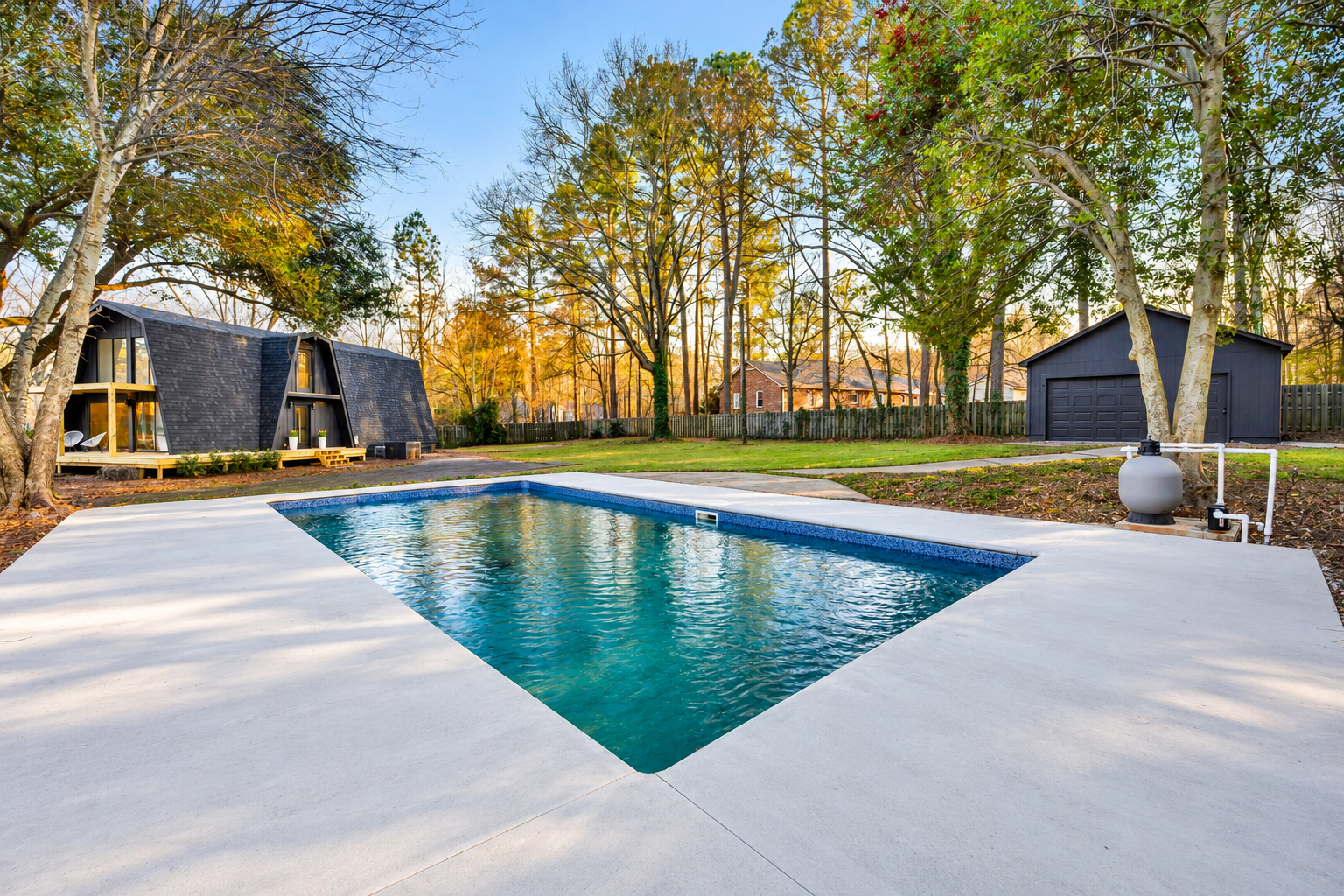 Renovated property at 112 Wayland Drive in Duncan, SC, featuring a modern in-ground swimming pool, spacious concrete patio, contemporary dark-sided home, and detached garage surrounded by mature trees.