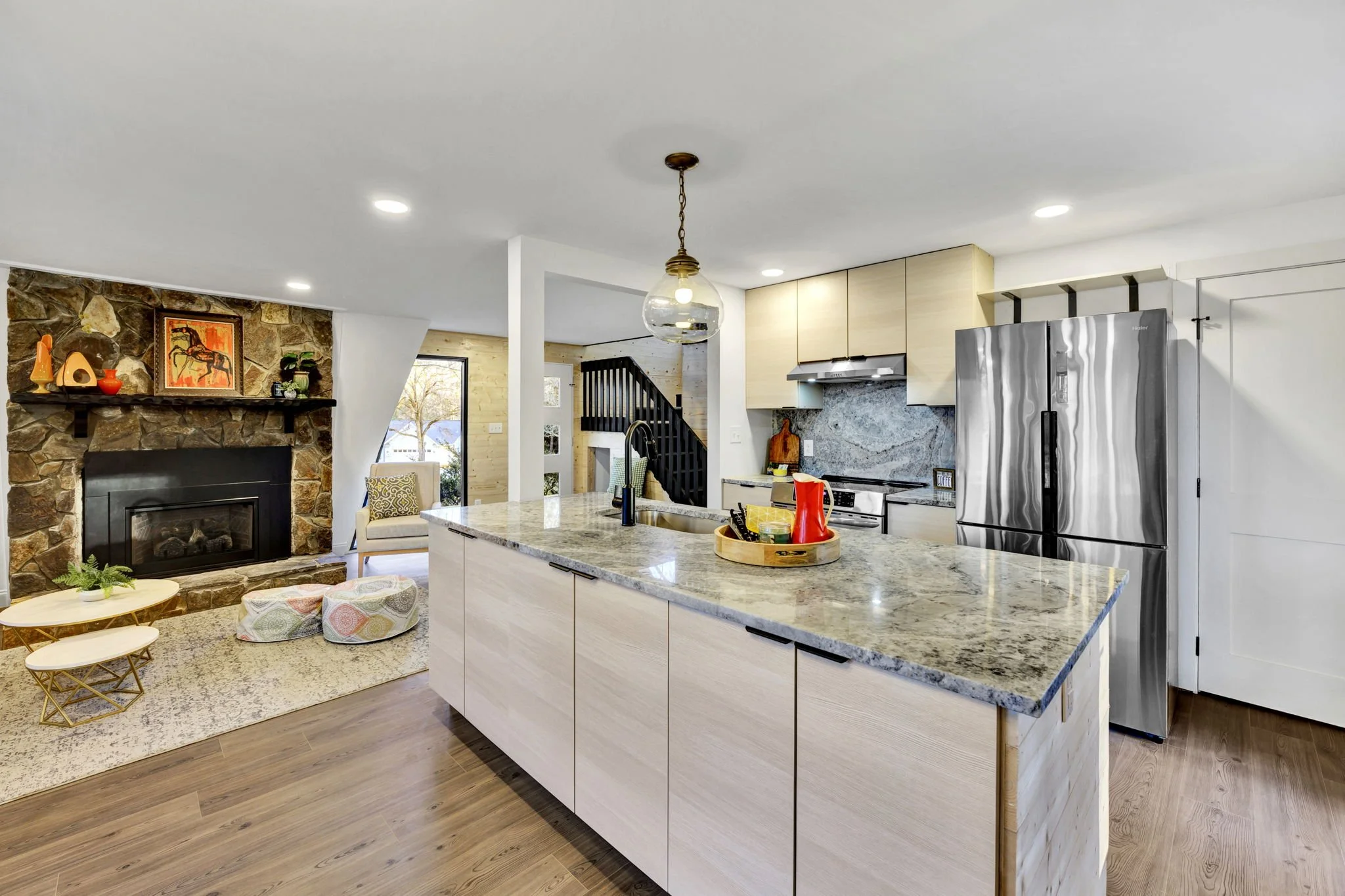Modern kitchen at 112 Wayland Drive in Duncan, SC, featuring a large stone-topped island, light wood cabinetry, stainless steel appliances, and an open-plan living area with a natural stone fireplace.