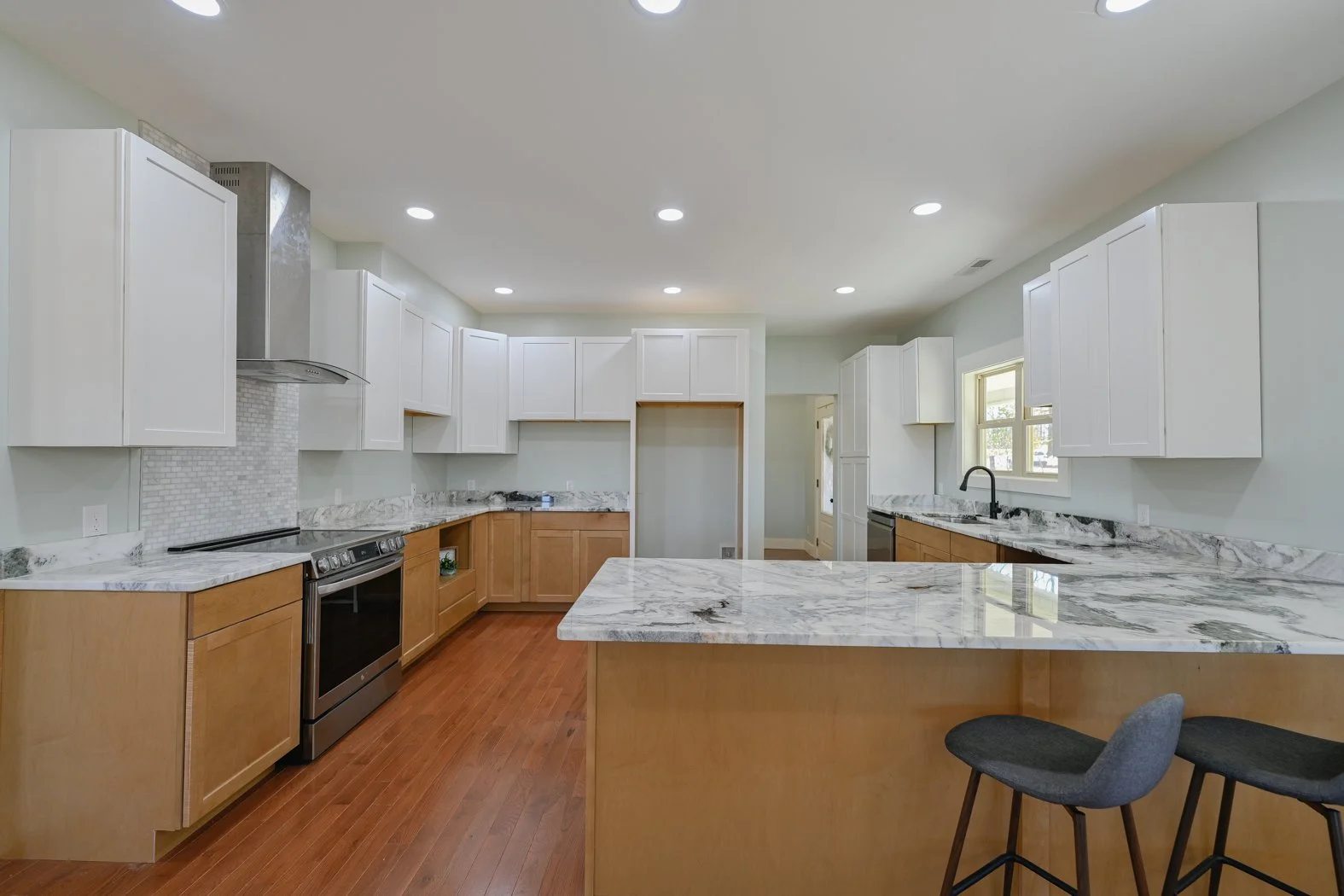 Renovated kitchen at 1334 Jameson Road in Easley, SC, featuring two-tone cabinetry, marble-look countertops, a large island with breakfast bar seating, stainless steel appliances, and hardwood floors.
