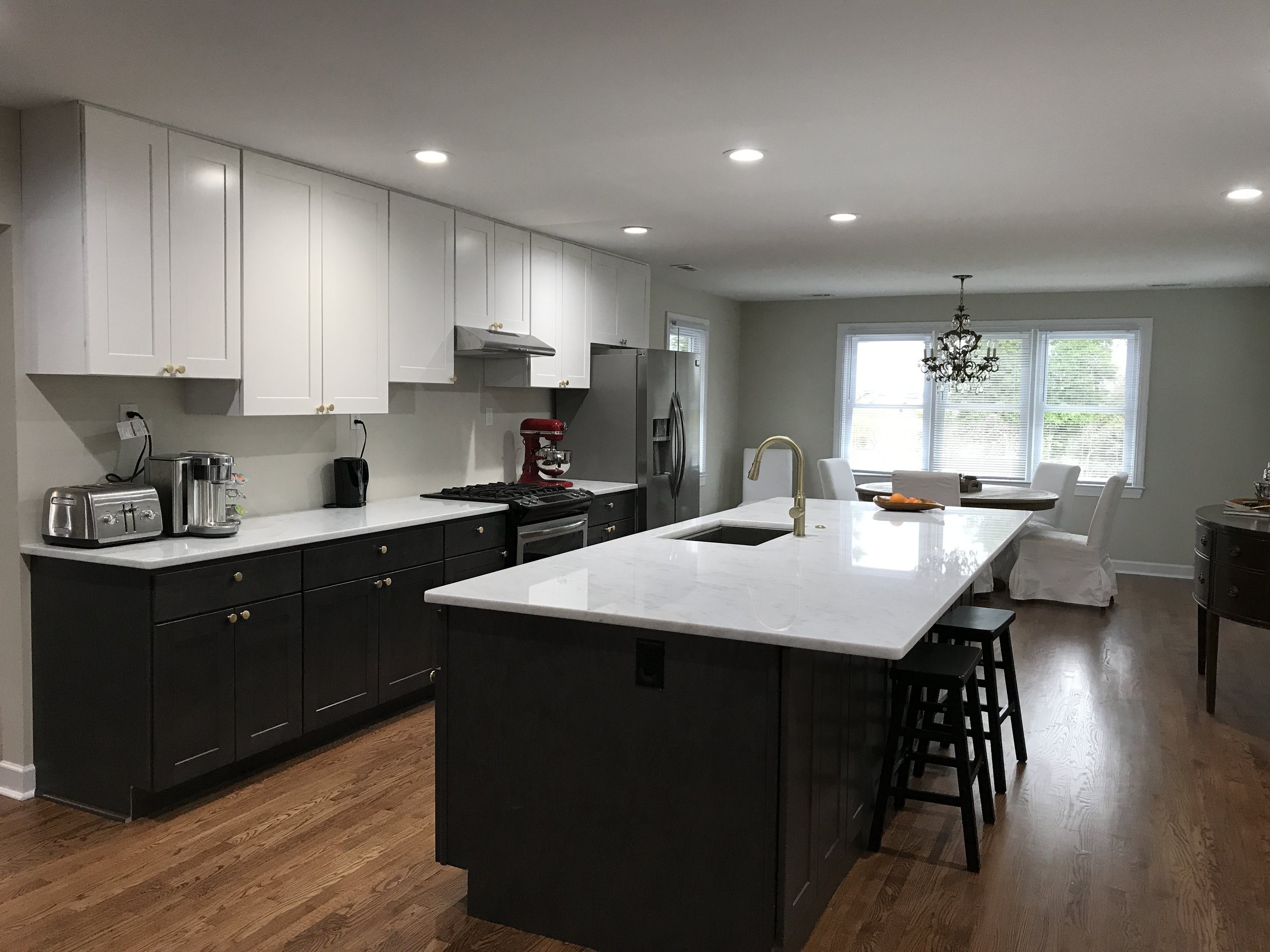 Renovated kitchen at 104 Medallion Lane in Lyman, SC, featuring two-tone cabinetry, a large quartz island with seating, brass fixtures, stainless steel appliances, and hardwood floors.