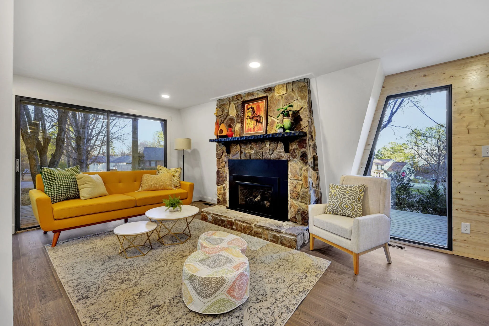 Renovated living room at 112 Wayland Drive in Duncan, SC, featuring a natural stone fireplace, expansive windows, wood flooring, and contemporary furnishings.