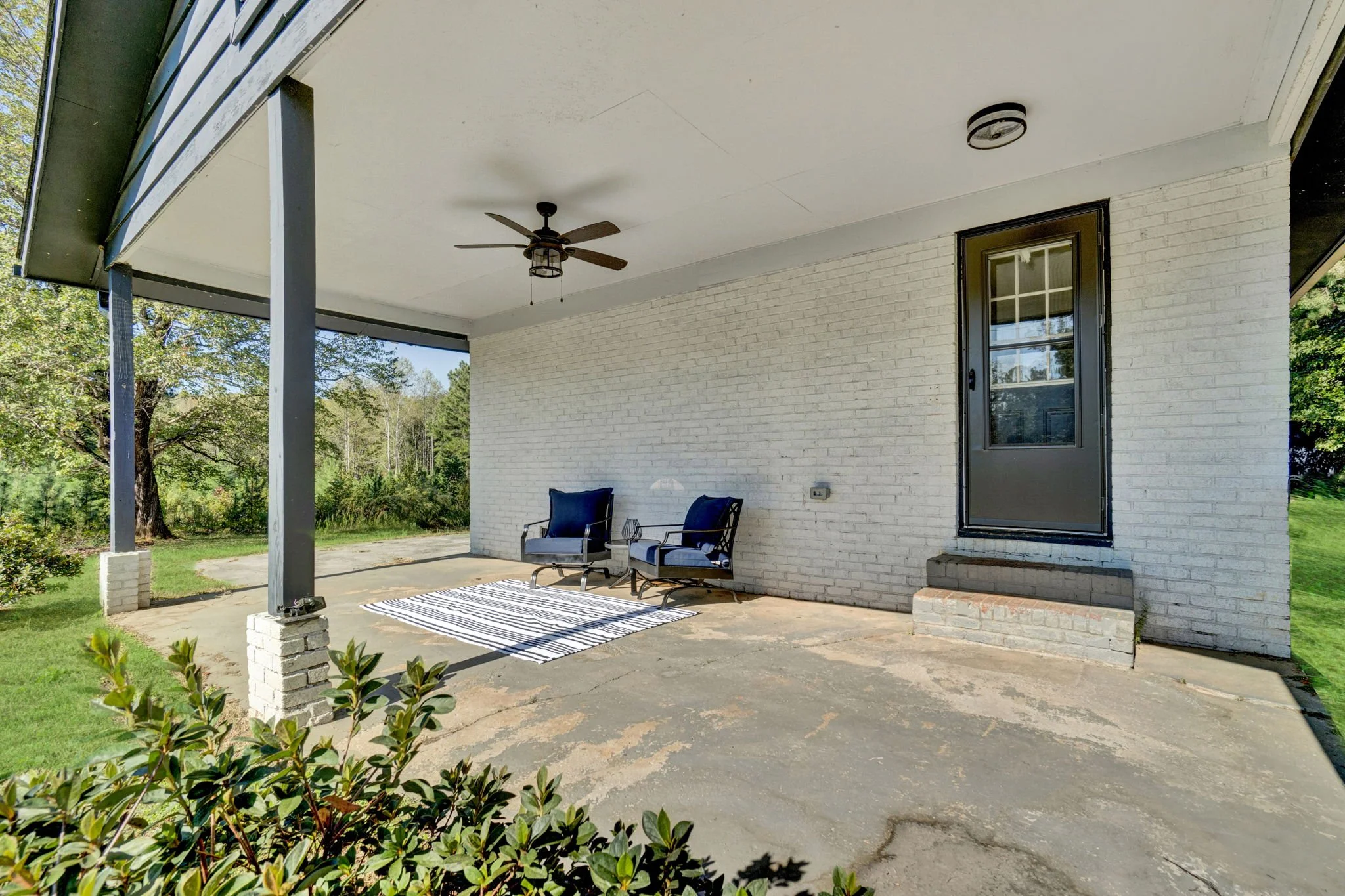 Renovated covered front porch at 1317 Hub Wilson Road in Landrum, SC, featuring white painted brick, dark support columns, outdoor seating, and views of the surrounding greenery.