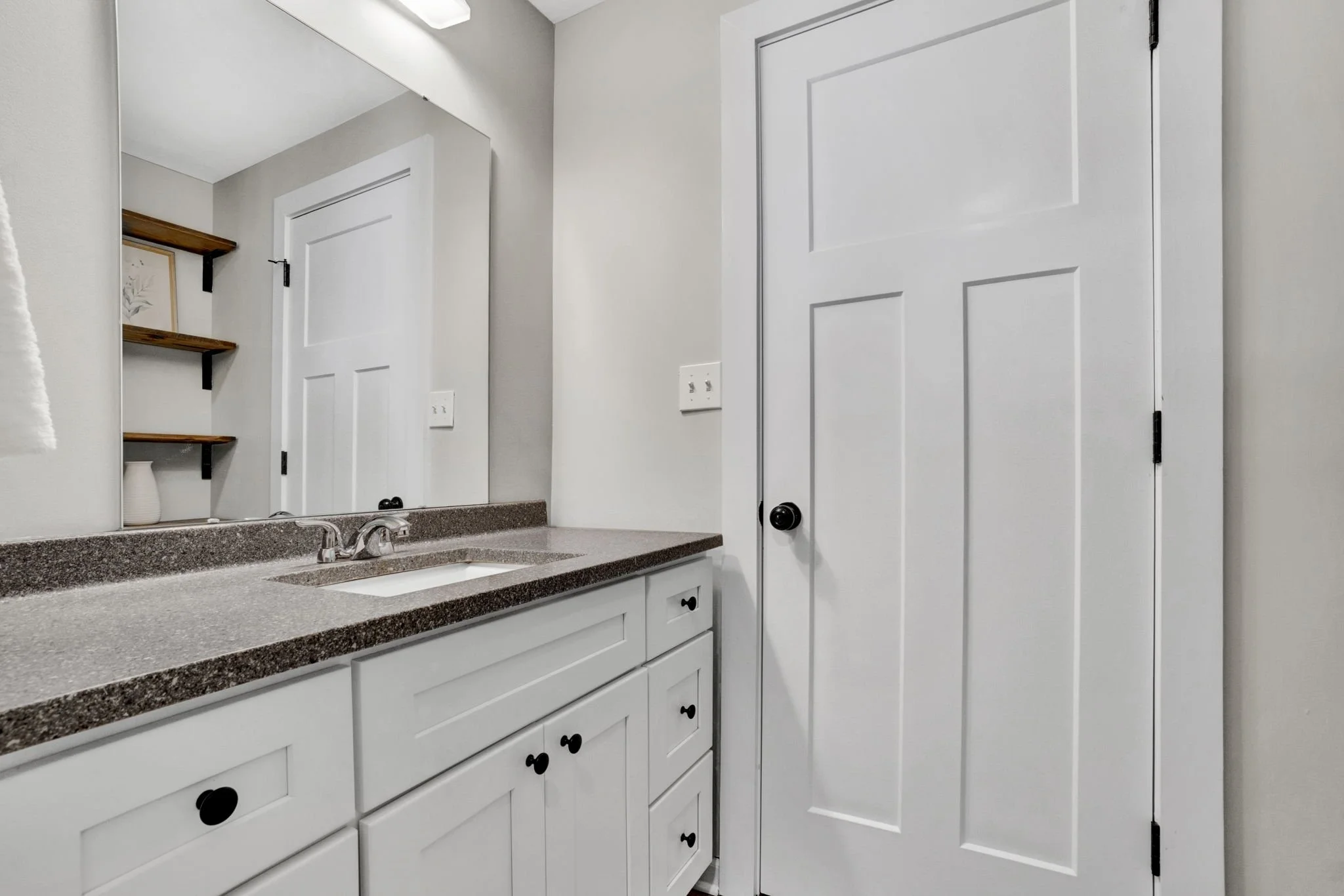 Renovated bathroom at 1317 Hub Wilson Road in Landrum, SC, featuring a white shaker-style vanity, granite countertop, large mirror, and open wood shelving.