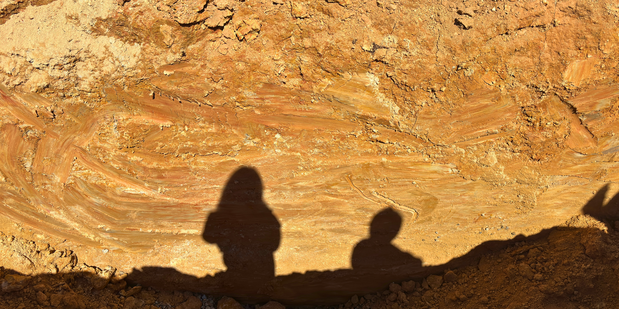 Shadows of two Red Dirt team members cast across exposed red clay at the Clinton Commons development site in Clinton, South Carolina.