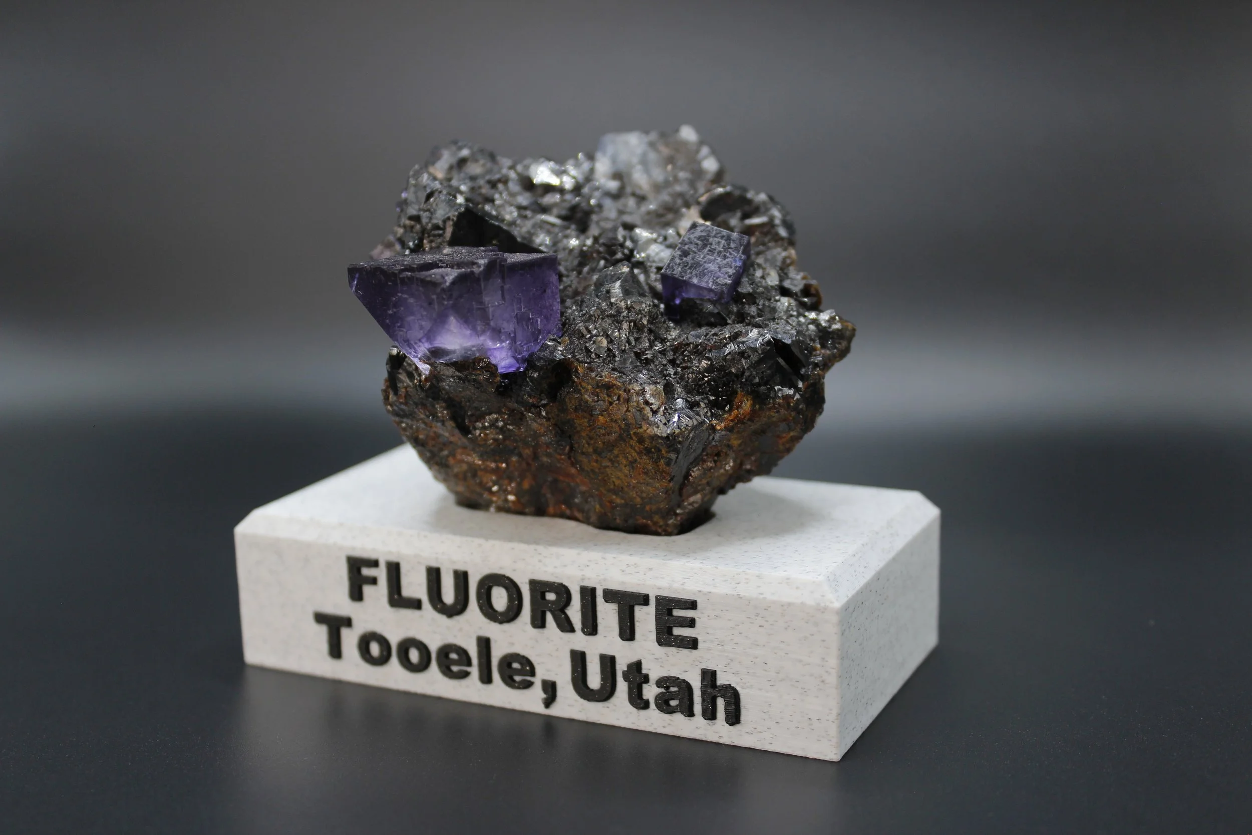 A sample of fluorite mineral from Tooele, Utah, with purple cubic crystals on a dark matrix.