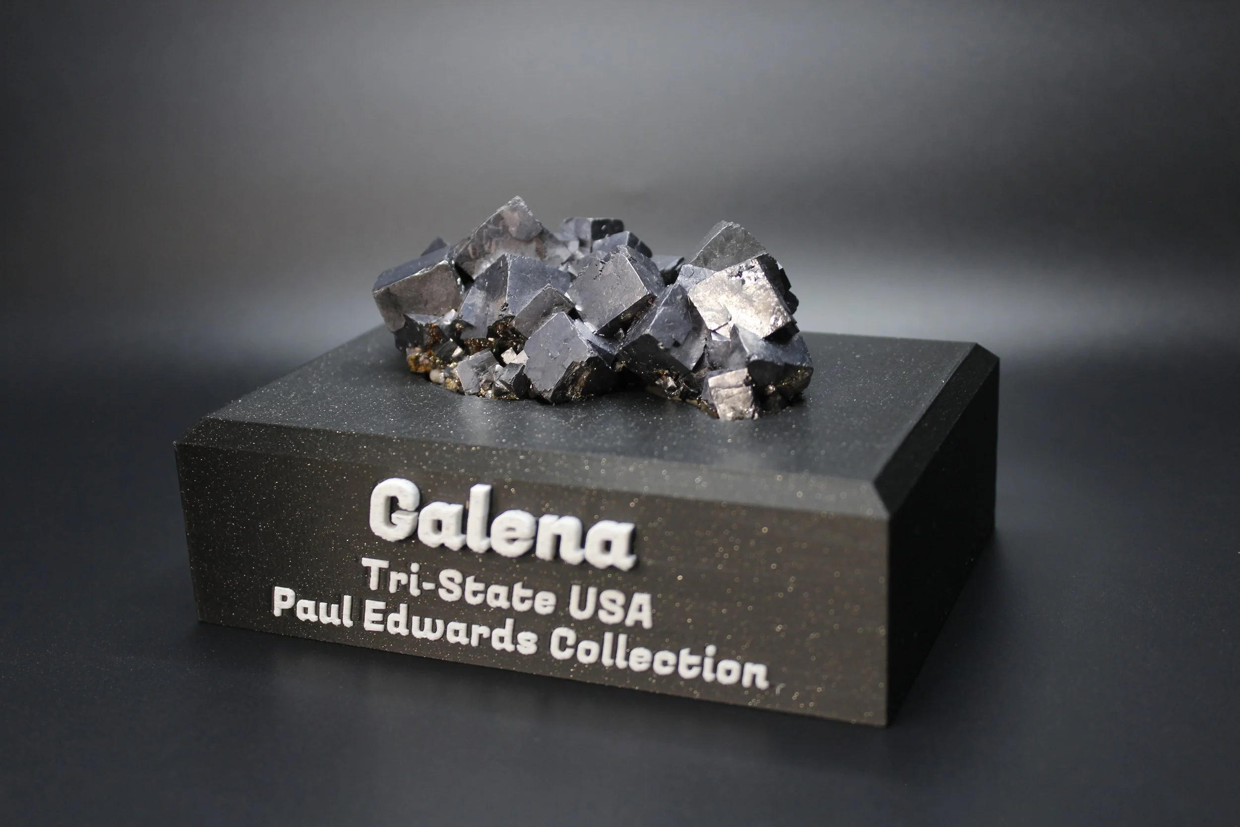 A mineral specimen of galena on a black display base with white text, indicating it is from the Tri-State USA and part of the Paul Edwards Collection.