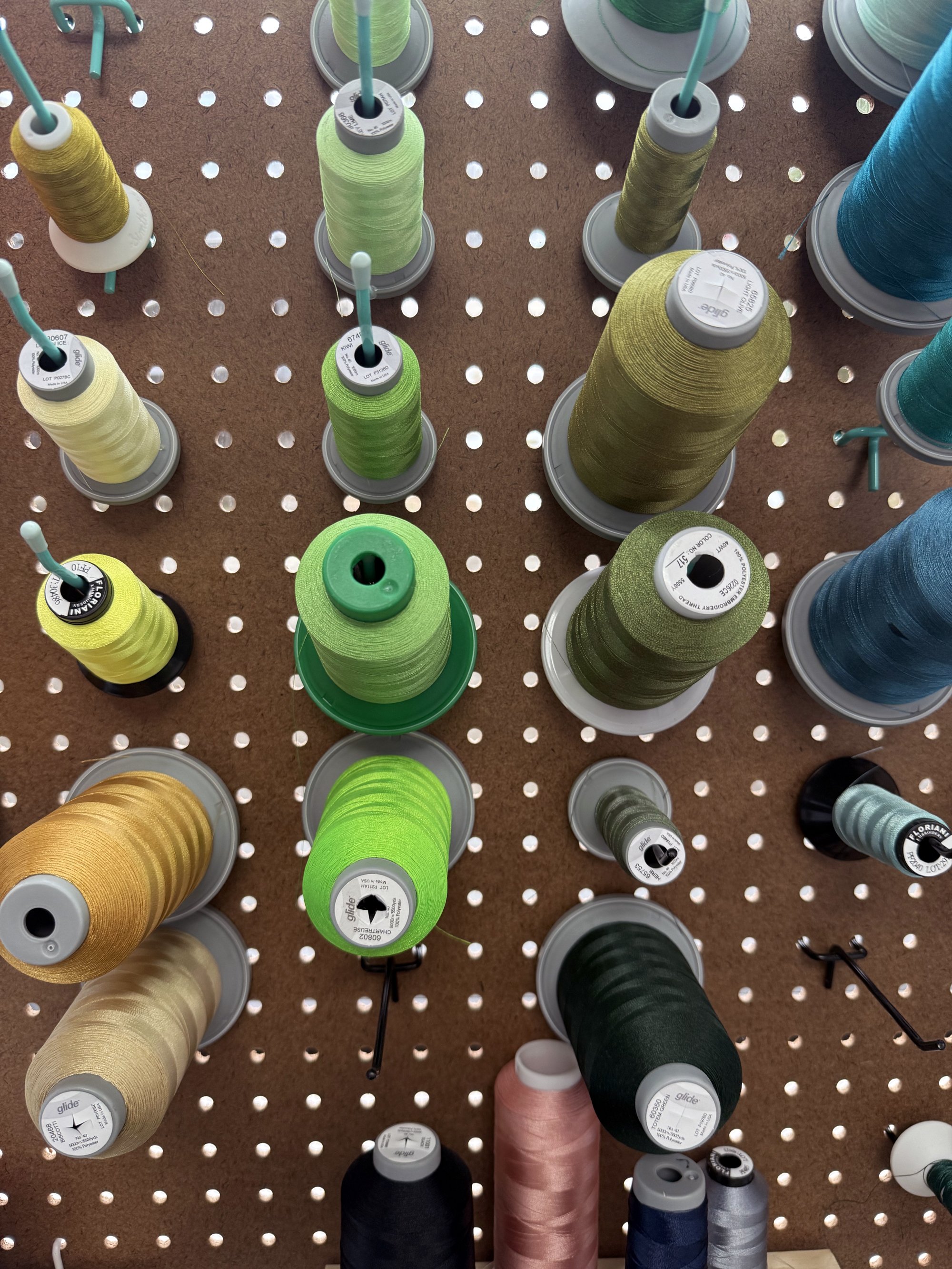 Spools of sewing thread in various colors arranged on a pegboard.