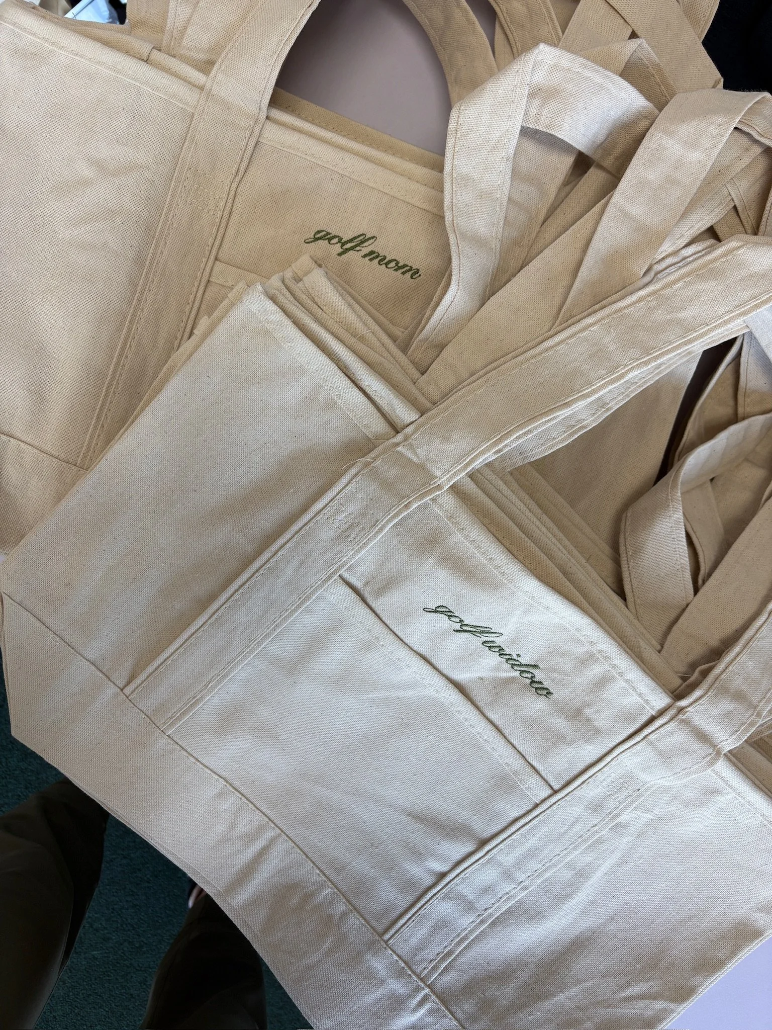 Cream-colored tote bag with 'golf mom' embroidered on it, containing matching totes.