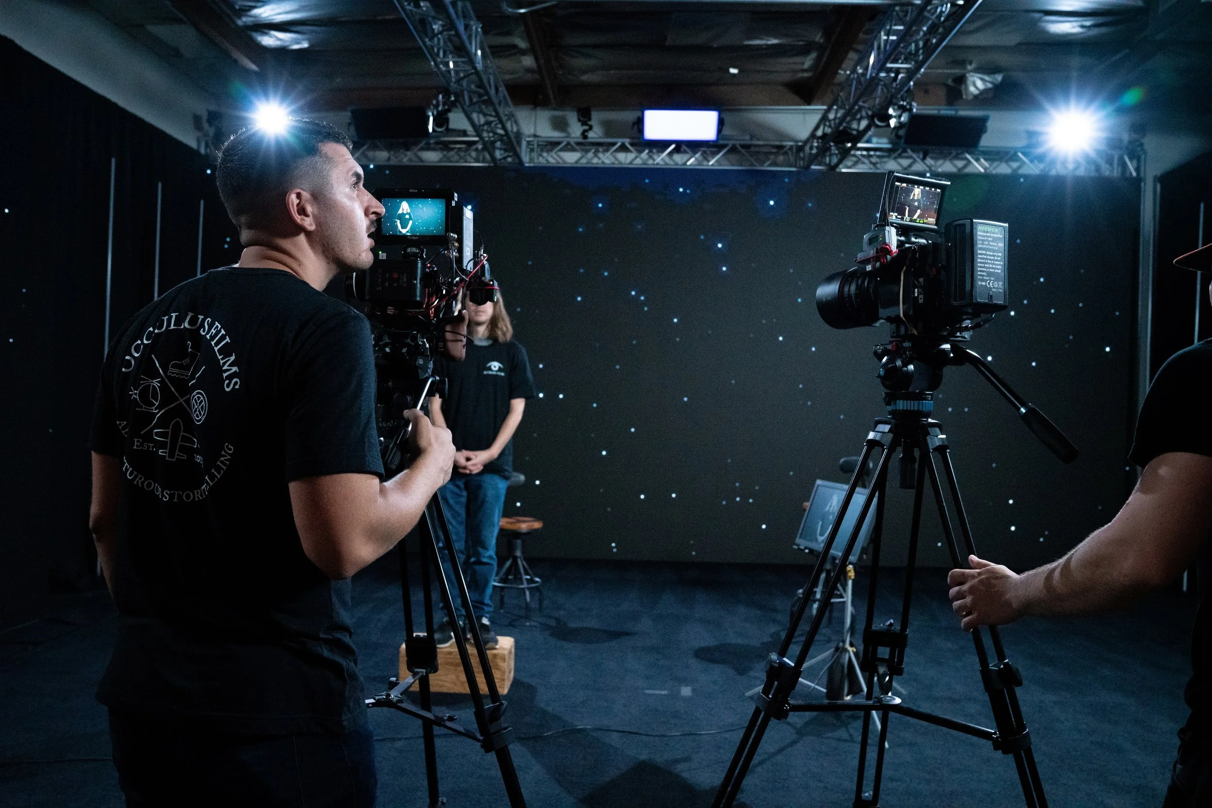 Filming crew operating cameras in front of a starry background on a dark stage.