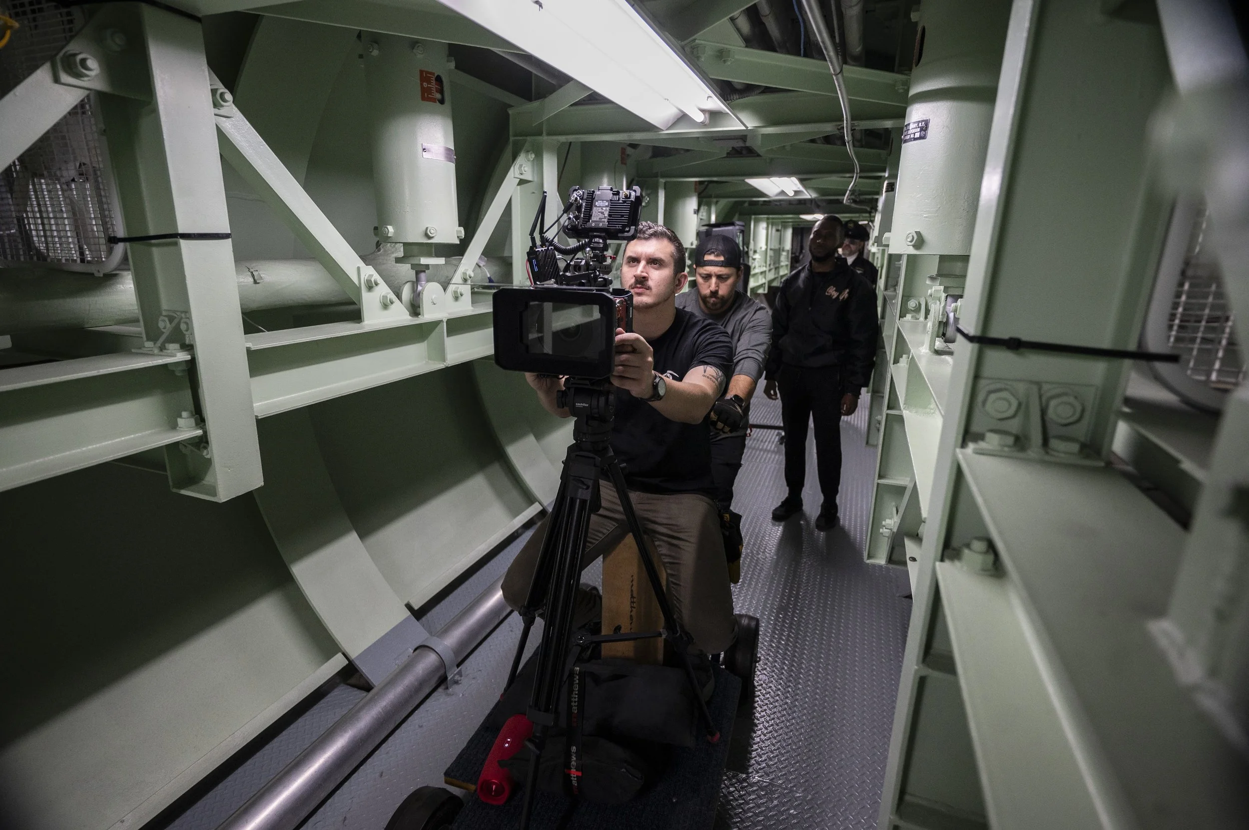 Filmmakers operate camera equipment inside a large, industrial green-colored mechanical or engineering structure.