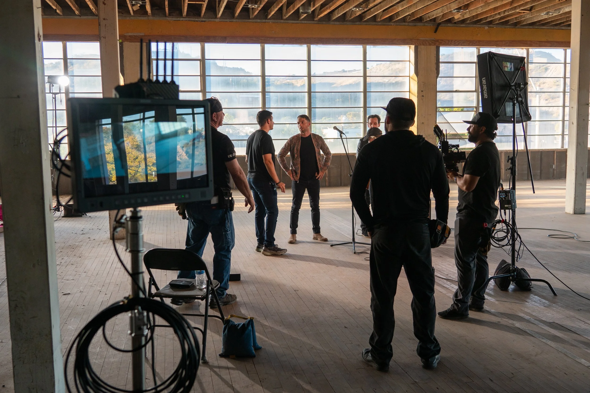 Film crew filming scene with actor in an industrial-style studio space with large windows and natural light.