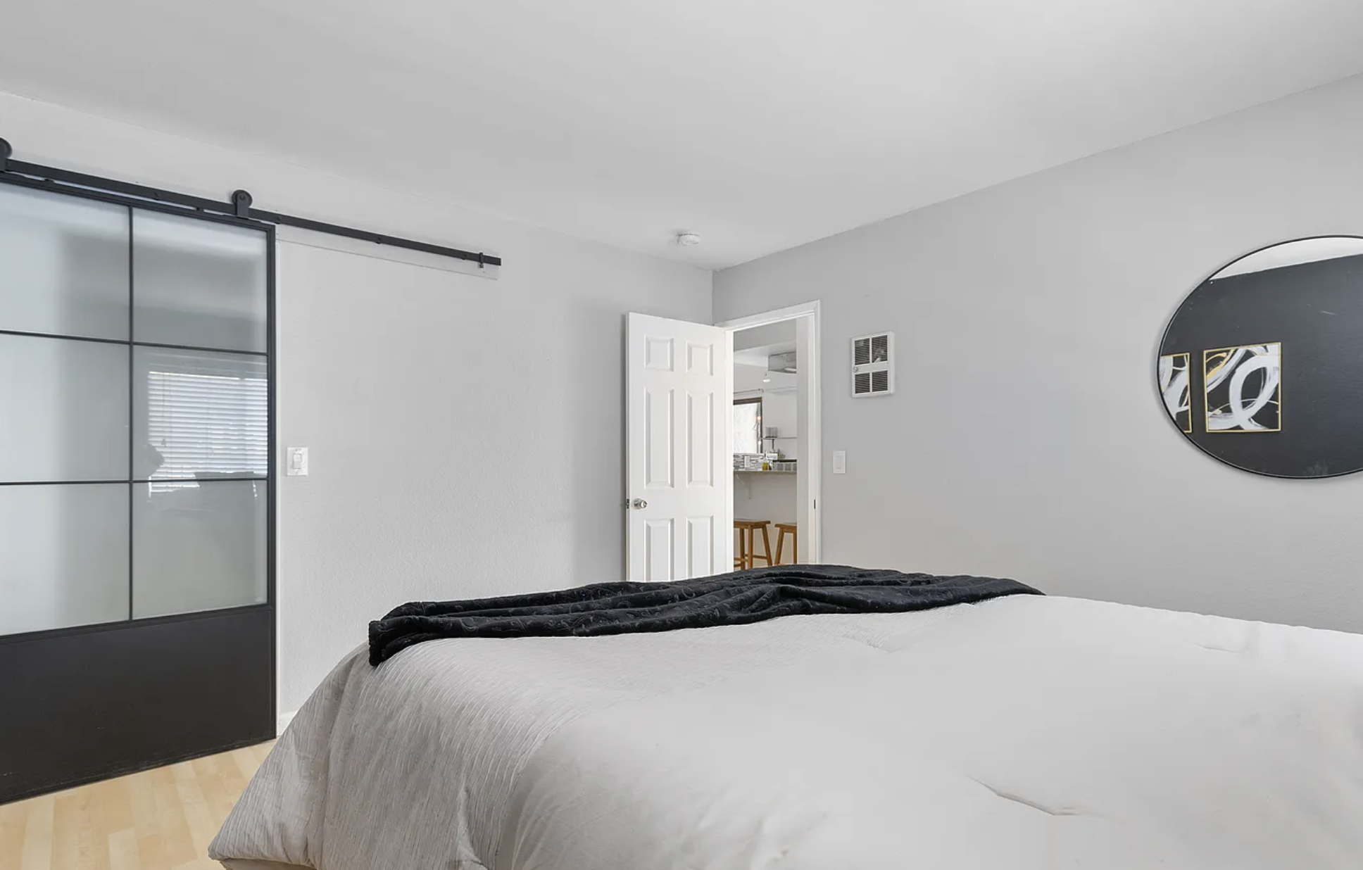 Minimalist bedroom with a bed, sliding glass door, open white door, round mirror, and wall art.