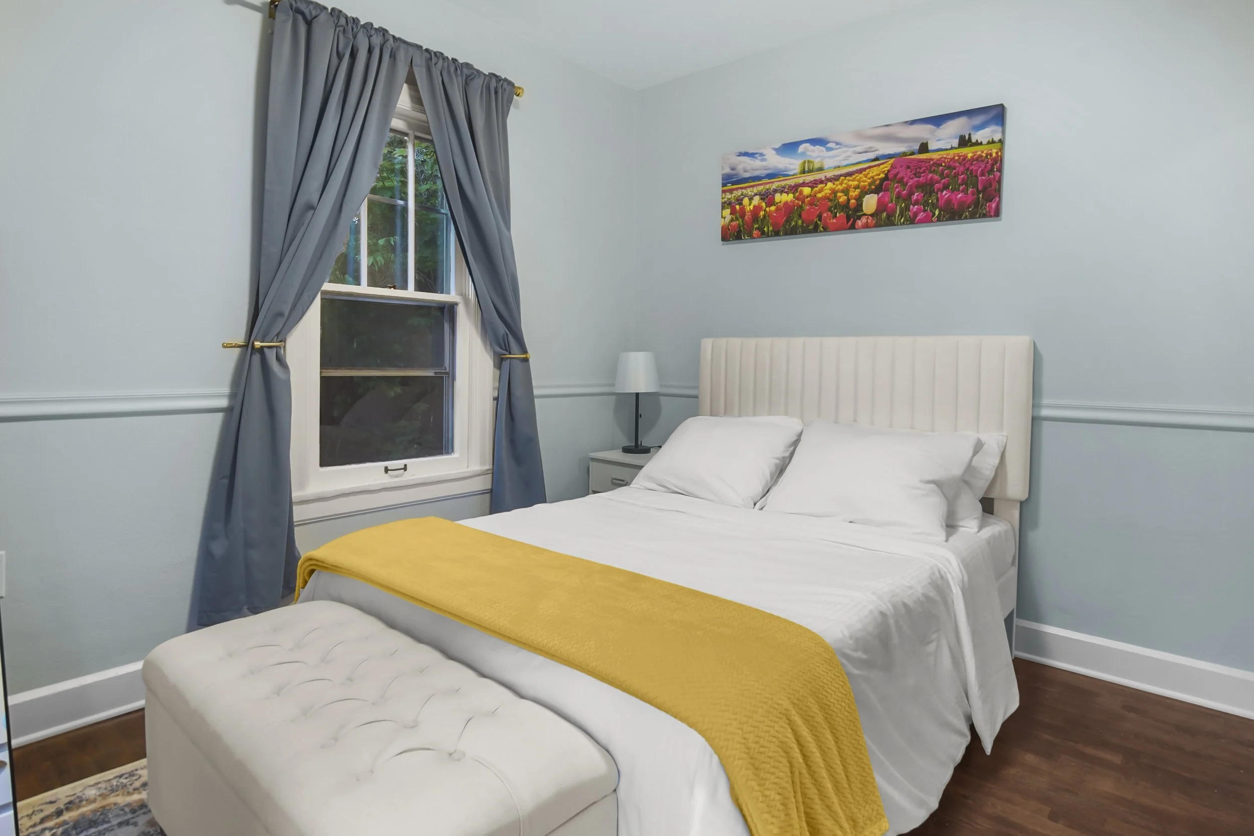 A lightly colored blue bedroom with a photo of the Washington State Tulip Festival.