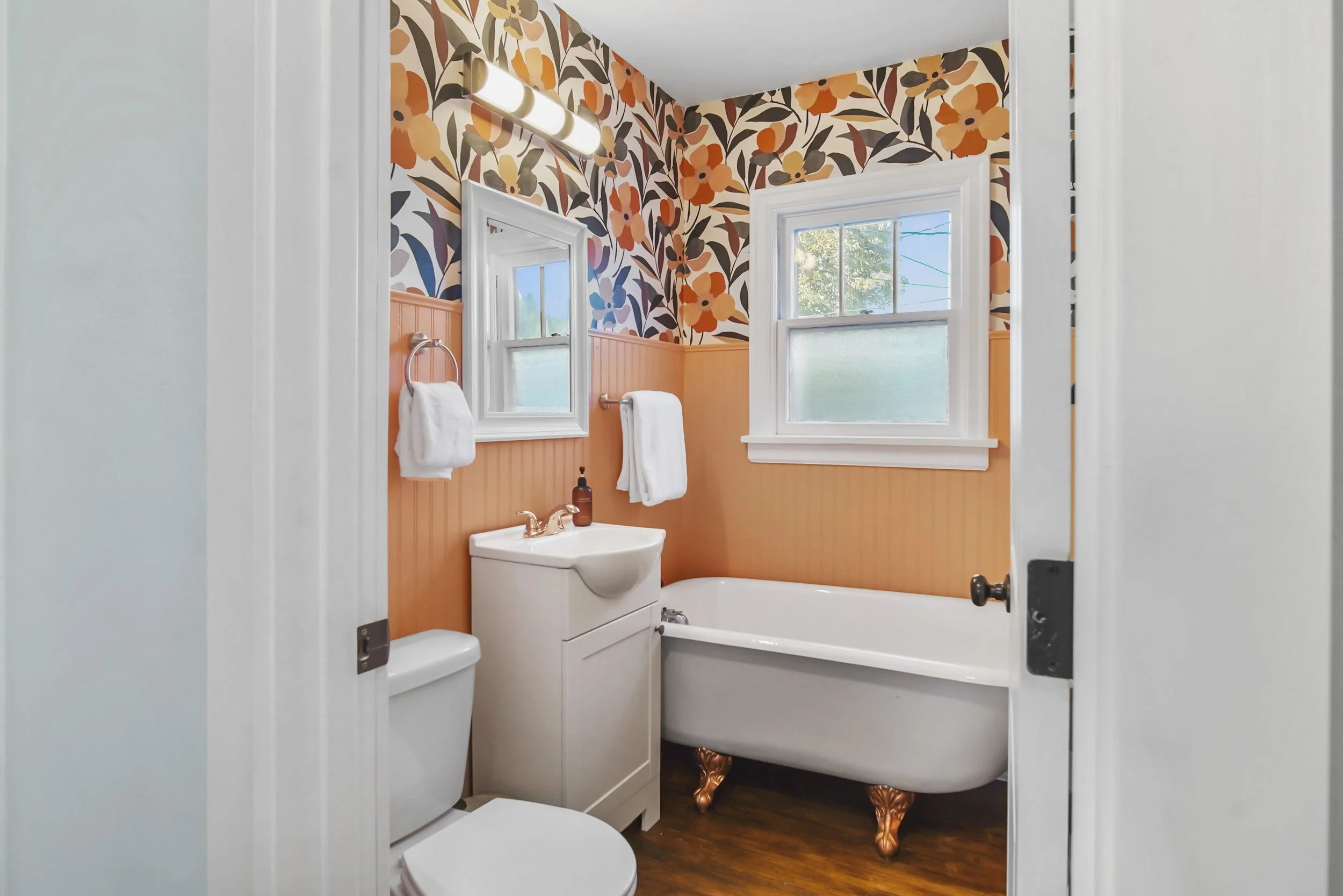 Brightly colored coral bathroom with shiplap and floral wallpaper, a clawfoot rub and luscious towels