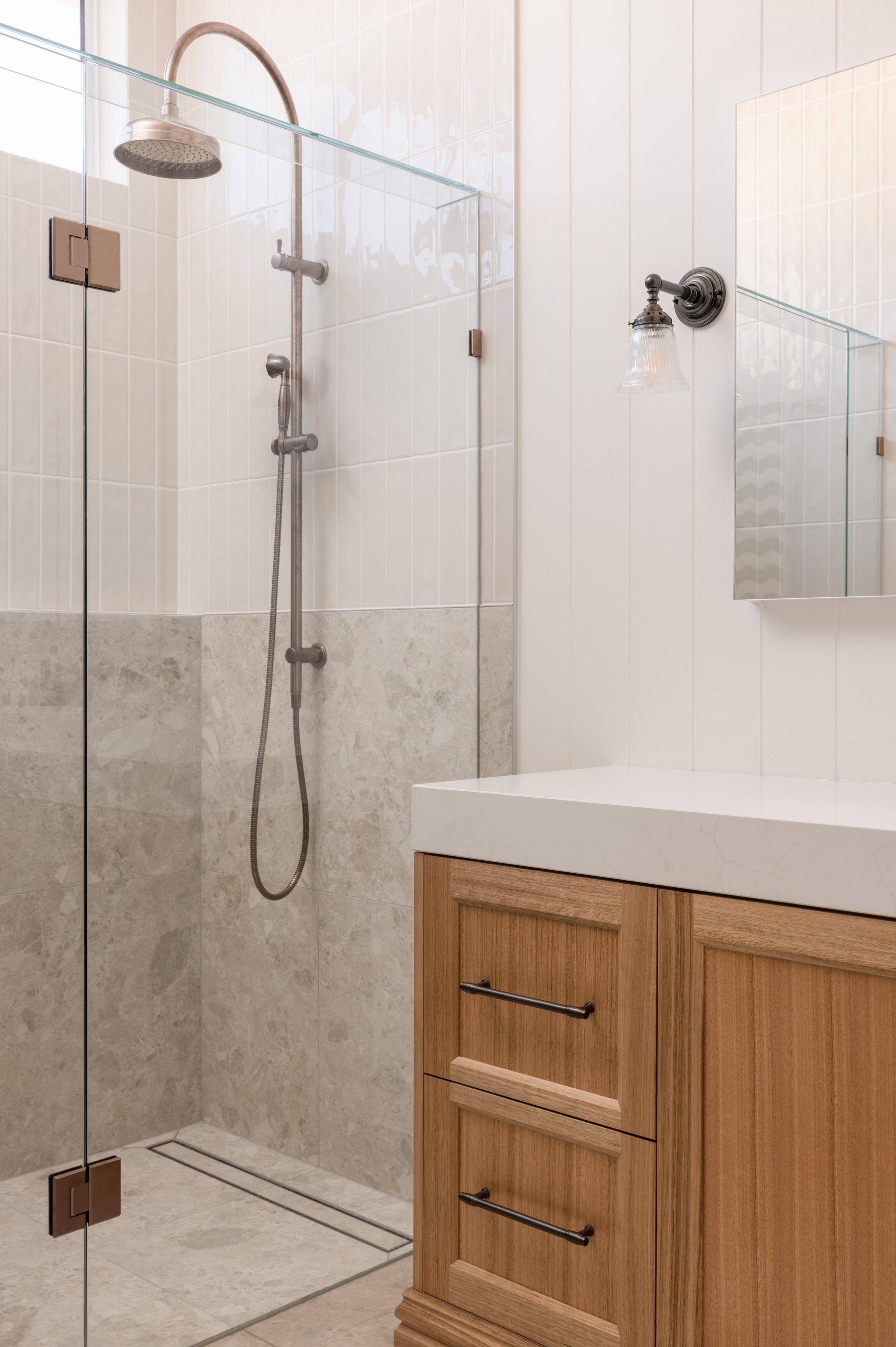 Modern bathroom with walk-in shower, glass door, beige tiles, wooden vanity with white countertop, and mirror.