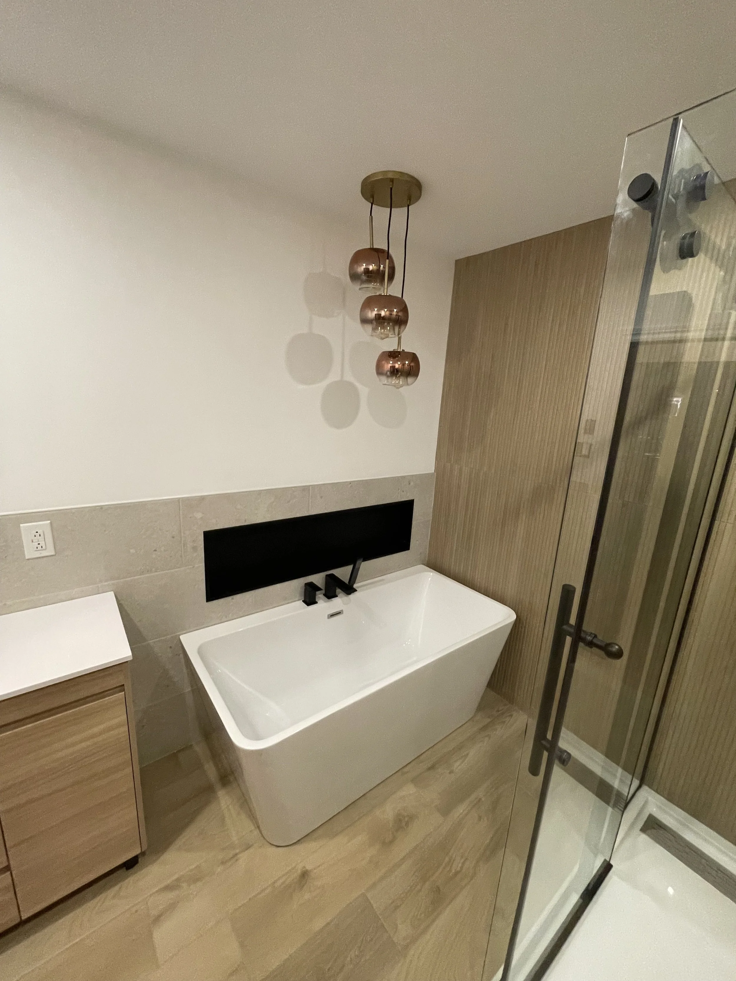 Modern bathroom with free-standing bathtub, wooden vanity, glass shower enclosure, and pendant lights.
