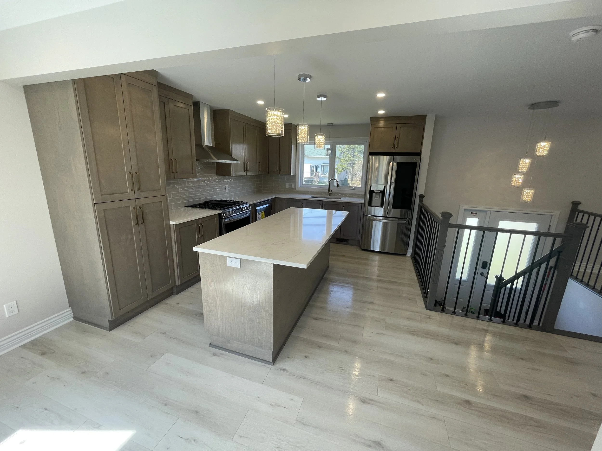 Modern kitchen with brown cabinetry, stainless steel appliances, a large kitchen island, pendant lights, and hardwood floors.
