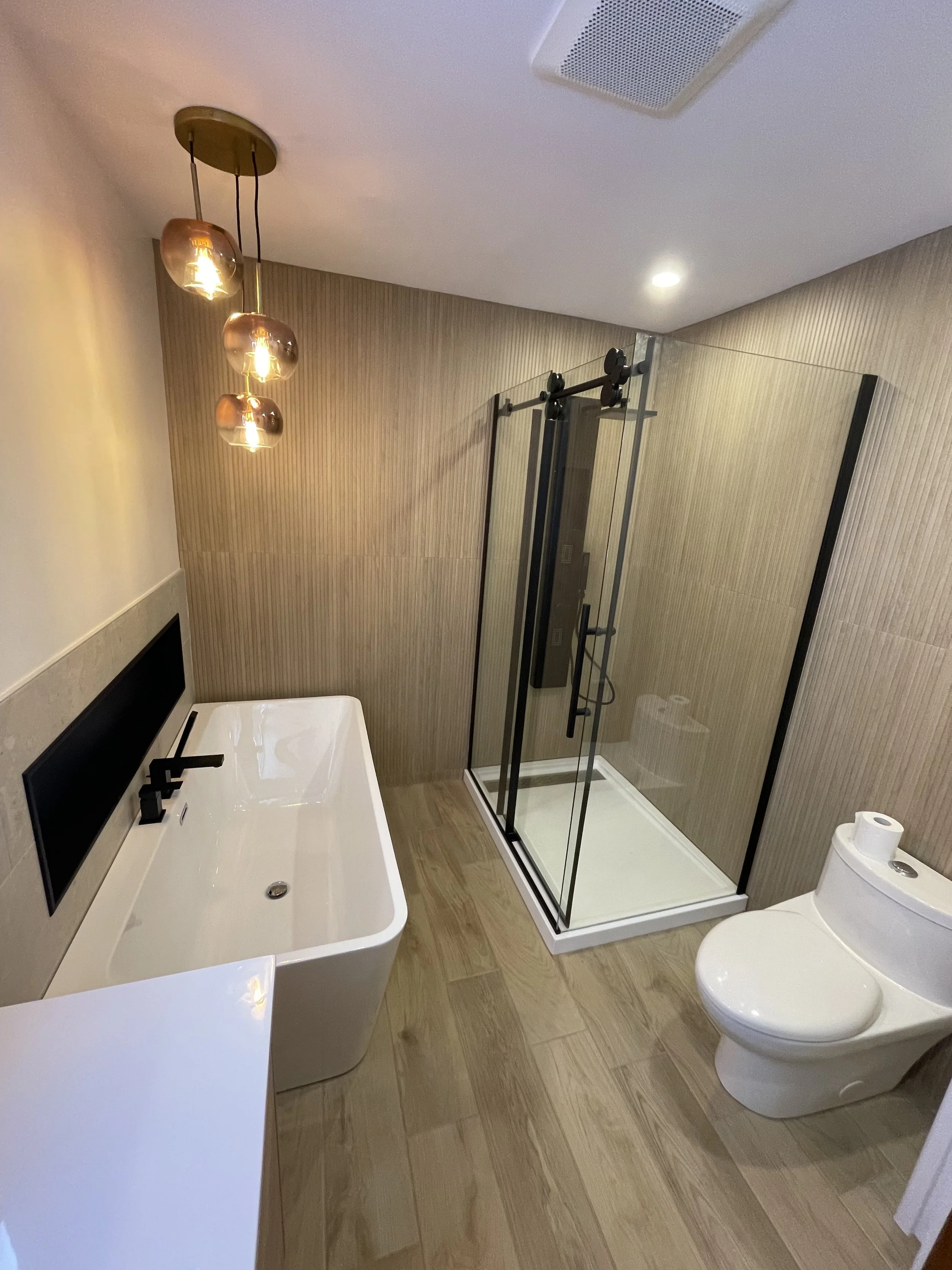 Bathroom with a white bathtub, a glass shower enclosure, a white toilet, and hanging light fixtures with three amber-colored glass shades.