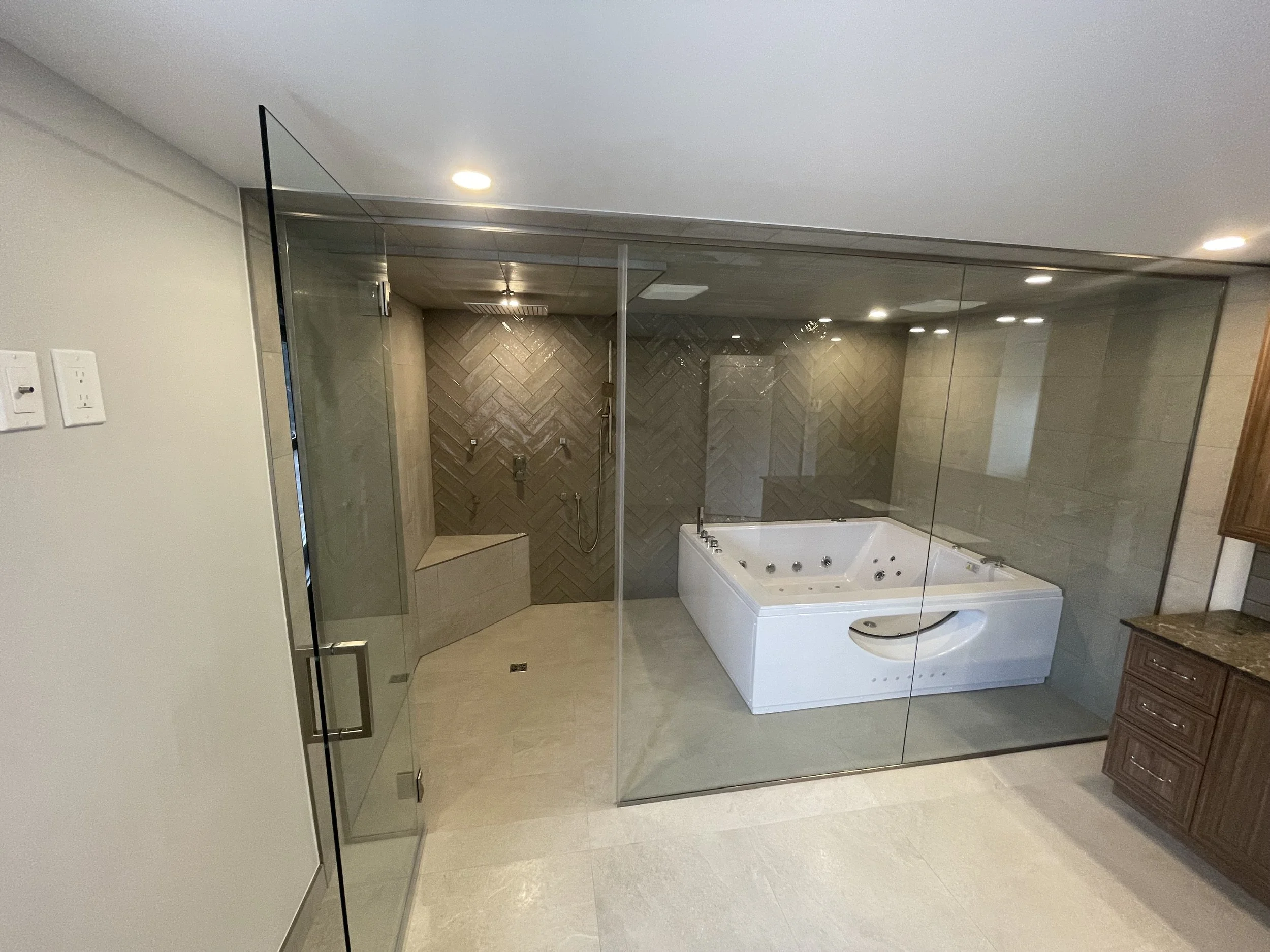 Bathroom with glass enclosure, walk-in shower with bench, and a large whirlpool tub, wooden cabinet with granite countertop.