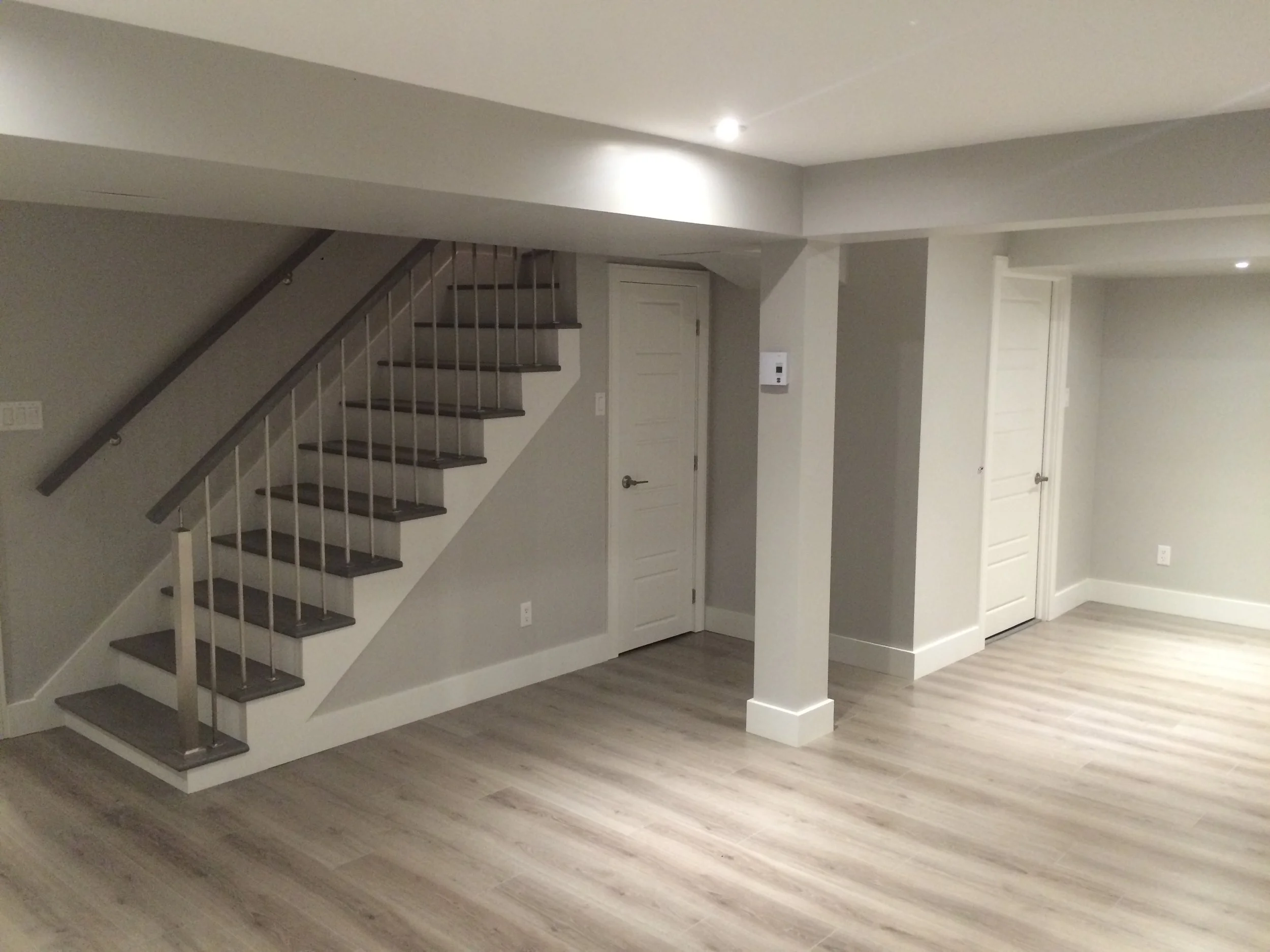 Empty living space with staircase, doors, gray walls, wood flooring, and recessed ceiling lighting.