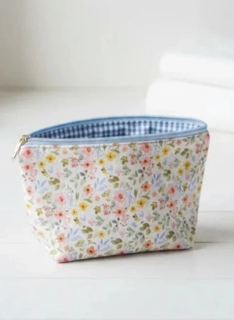 A floral fabric zippered pouch with a blue and white checkered interior, sitting on a white surface.