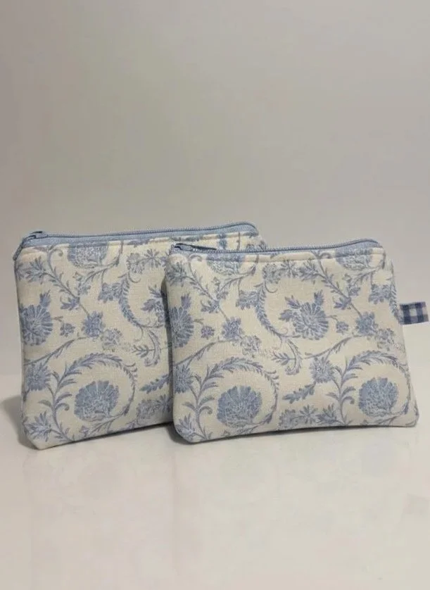 Two matching fabric pouches with blue floral patterns, one larger with a zipper, and one smaller with a side loop, placed on a white surface against a light gray background.