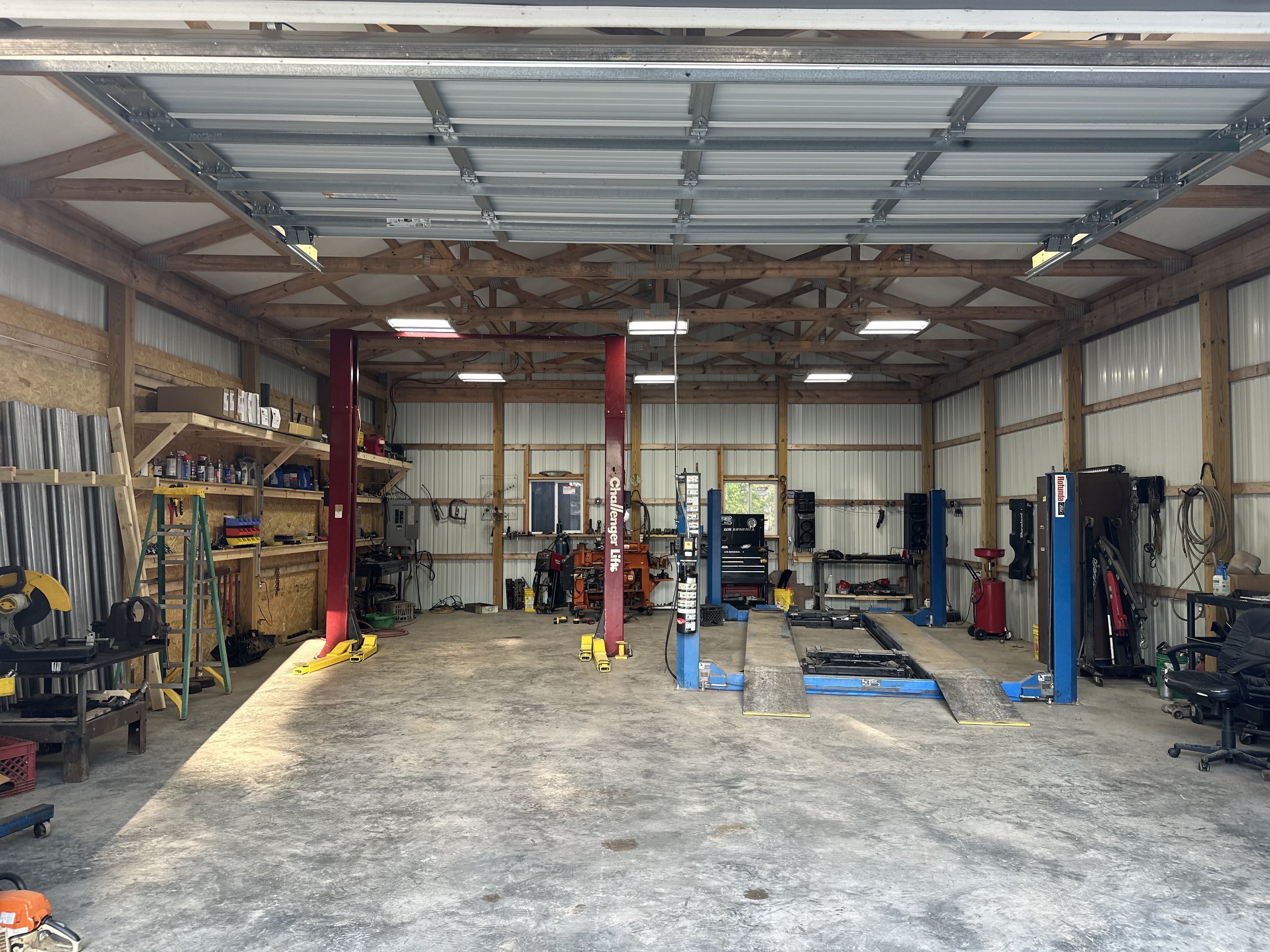 Inside a garage workshop with a car lift, shelves with tools, and various equipment.