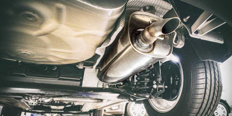 Underneath a car showing the exhaust system, muffler, and rear wheel.