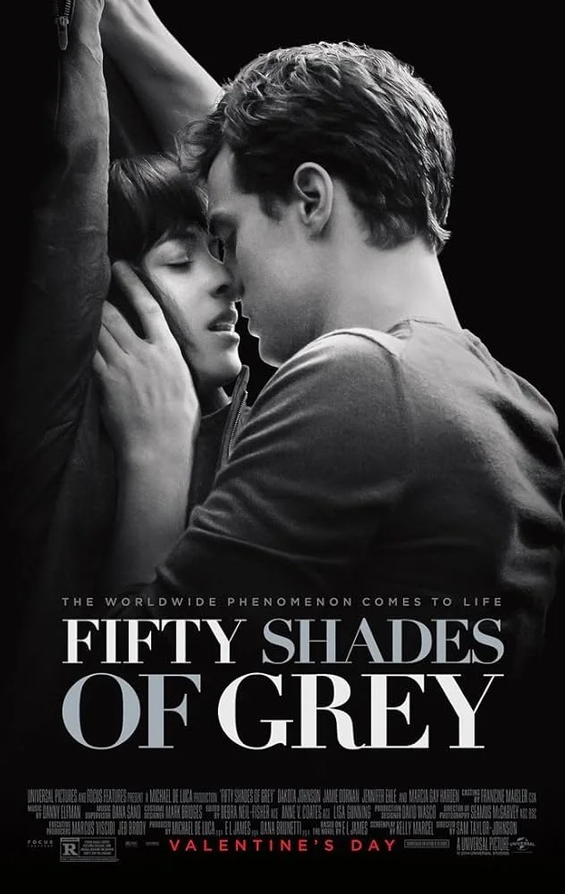 Black and white poster for the movie "Fifty Shades of Grey" showing a close-up of a man and woman touching foreheads, with the man holding the woman's face. The title "Fifty Shades of Grey" is prominently displayed, along with the tagline "The worldwide phenomenon comes to life" and mention of Valentine's Day.
