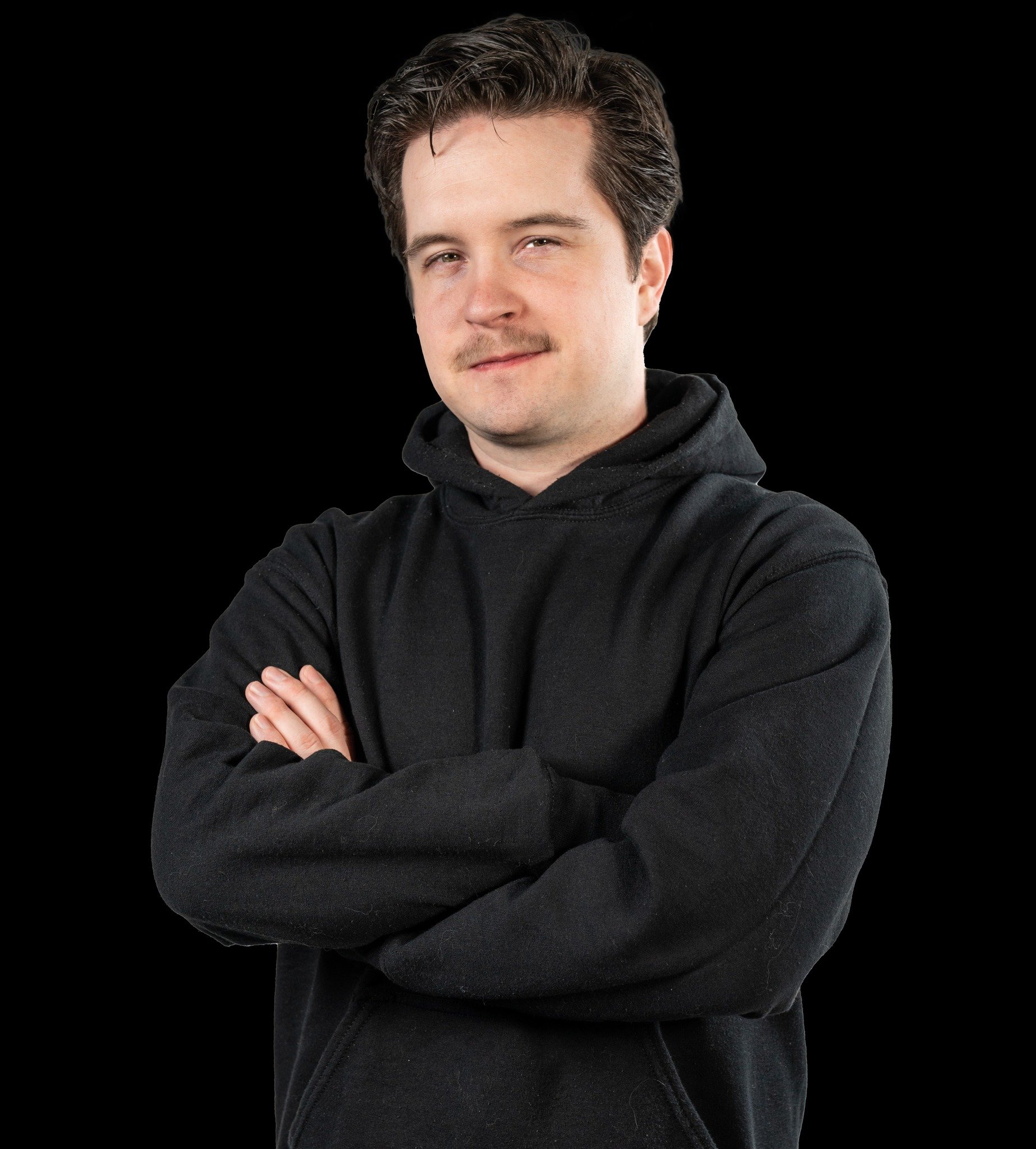 A media guy with dark hair in a black long-sleeve shirt, smiling with arms crossed against a plain background.