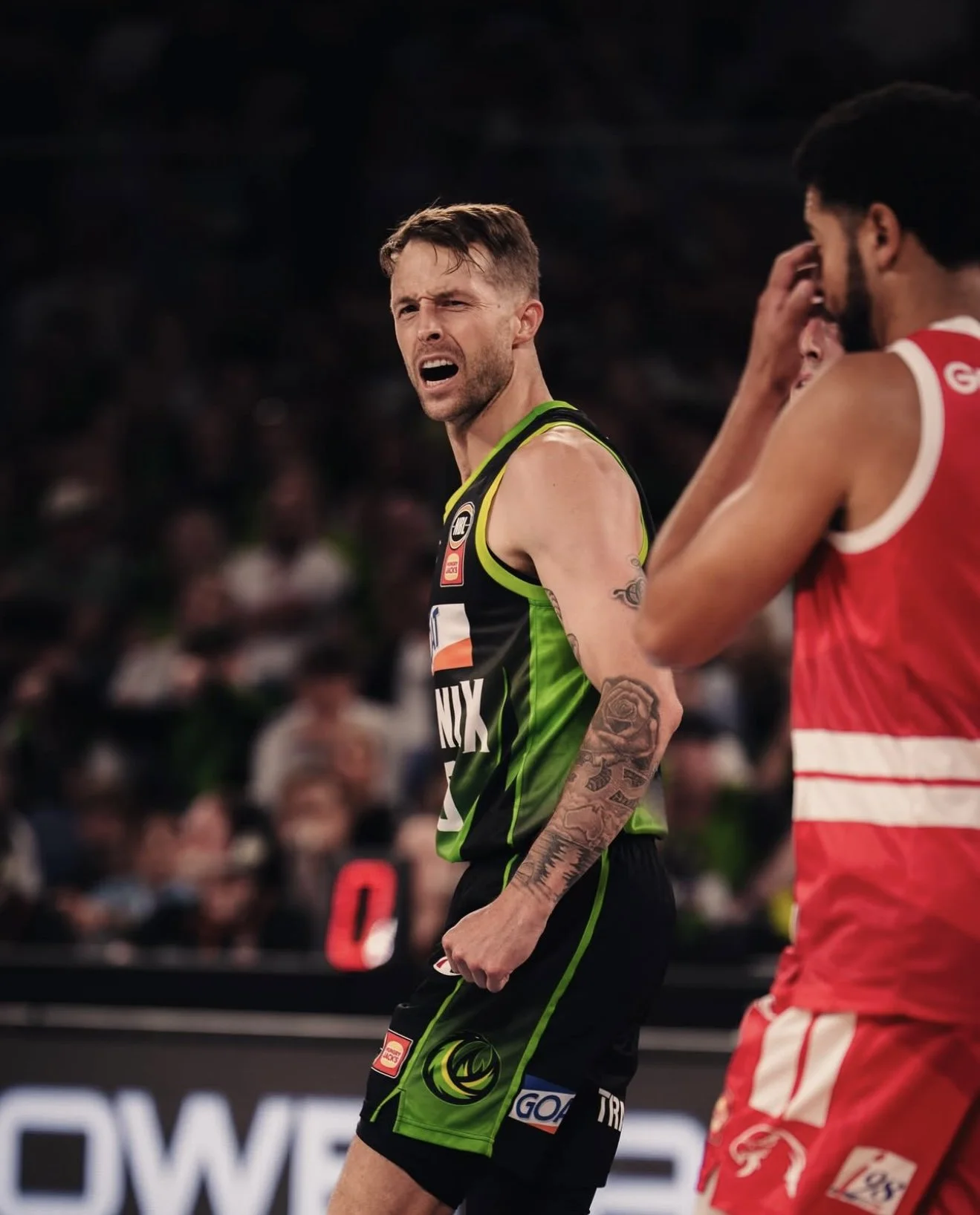A basketball player in a black and green uniform is holding his stomach and appears to be in pain, while another player in a red uniform is touching his face during a game.