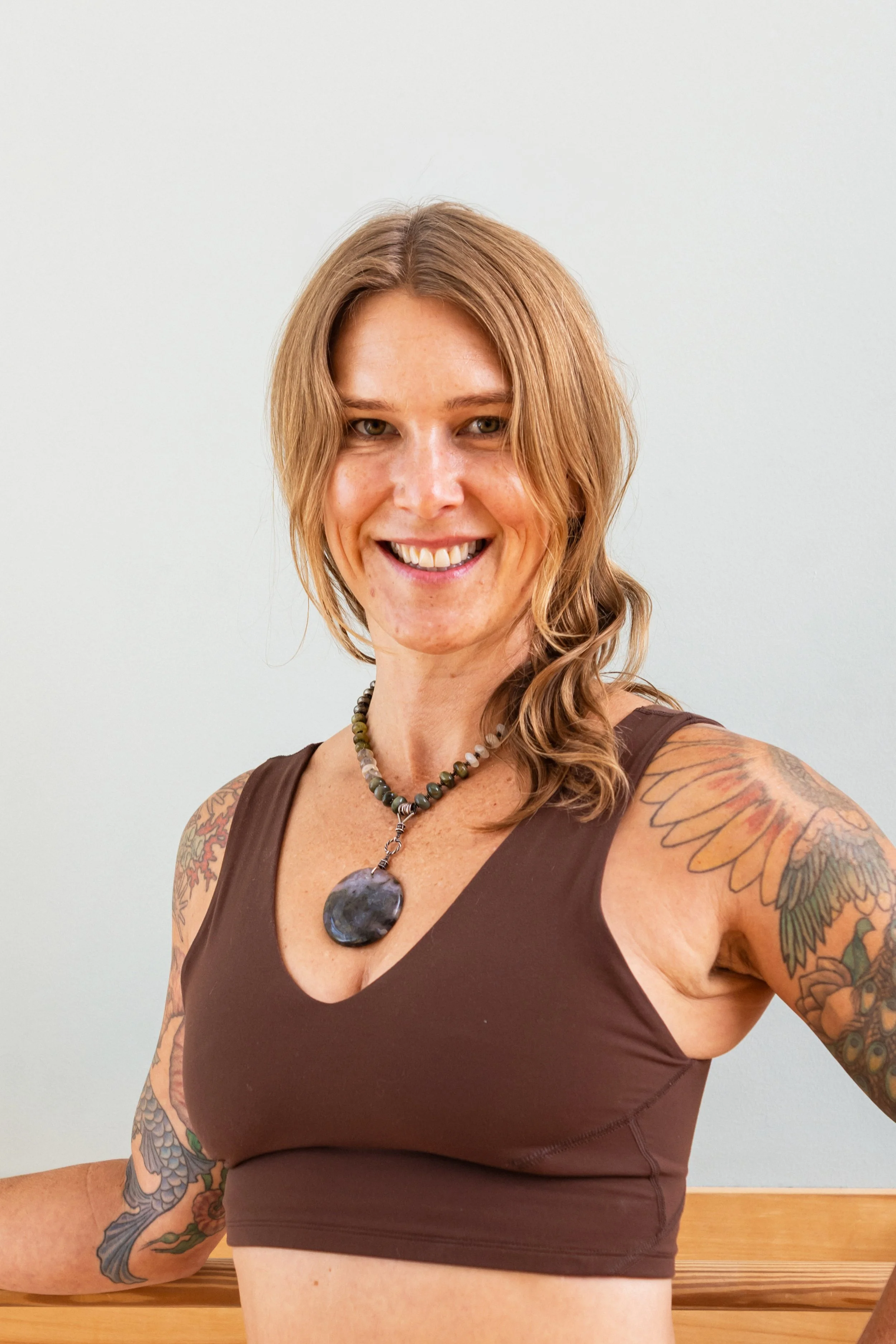 A woman practicing yoga or meditation indoors, sitting in a cross-legged pose on wooden flooring near a large potted plant and a window.
