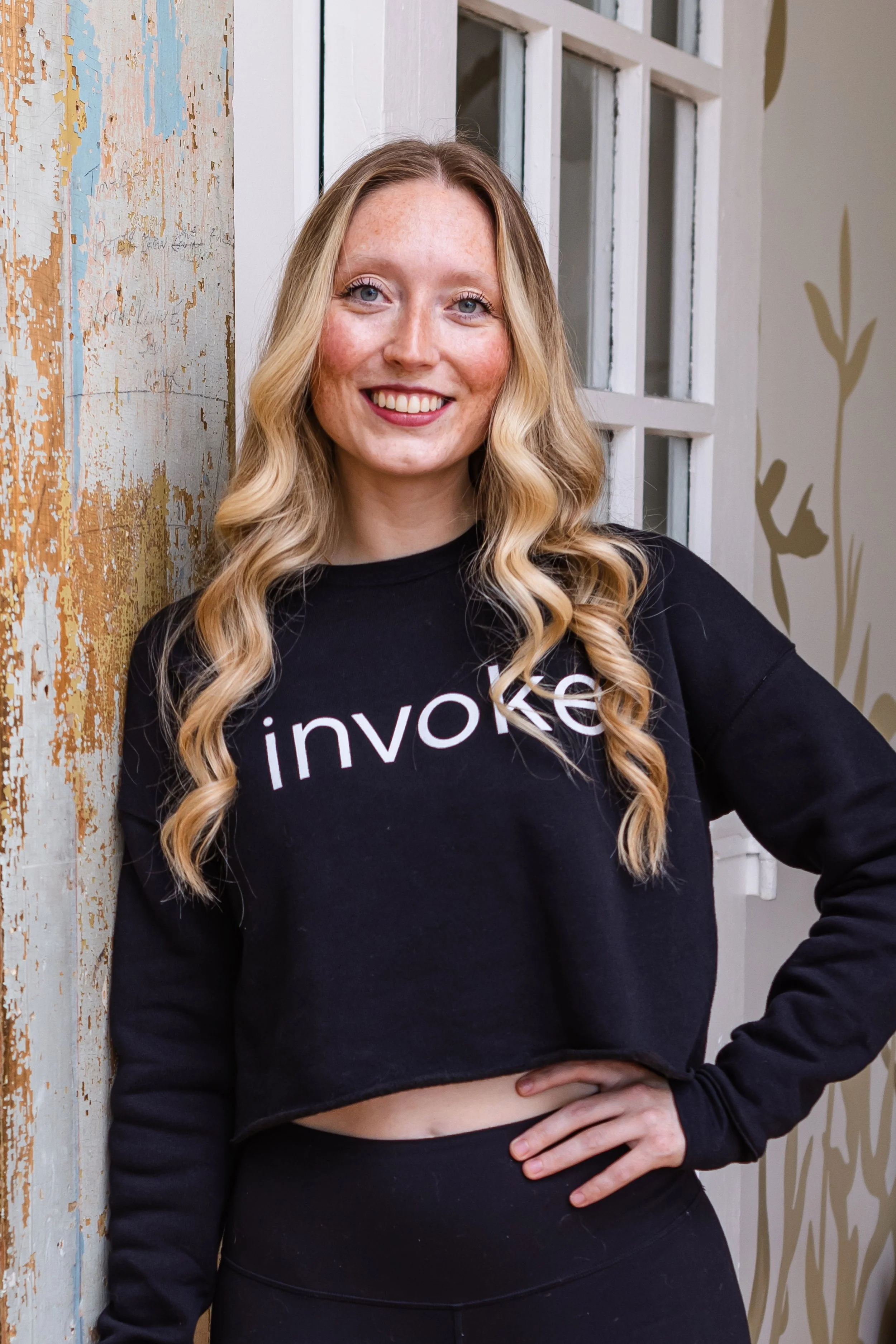 A woman in workout attire performing a boat pose on a yoga mat in a fitness studio, smiling at the camera.