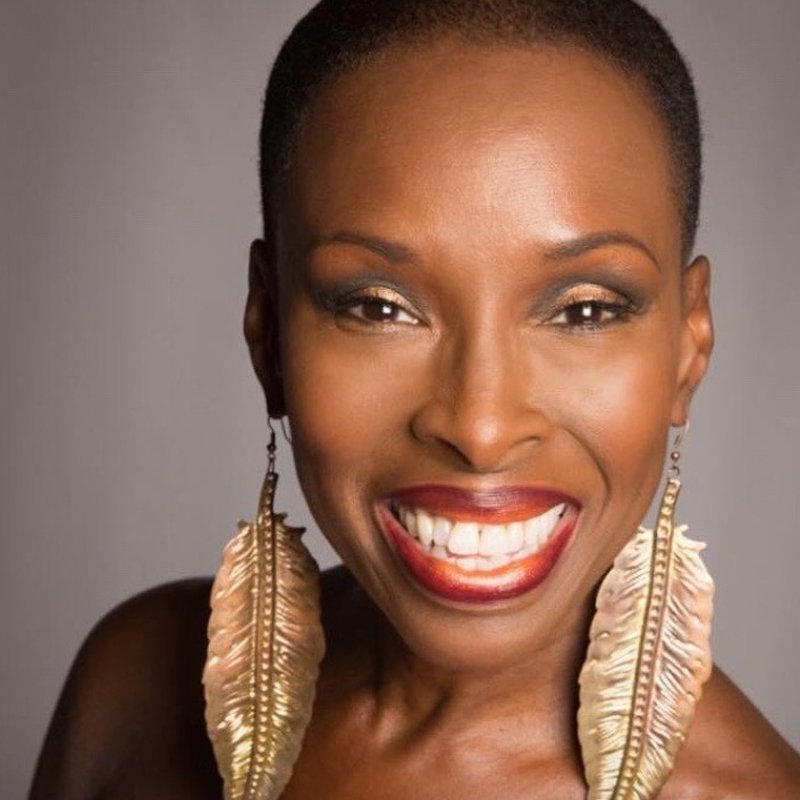 Close-up portrait of a smiling African American woman with short hair, wearing gold feather earrings and makeup.