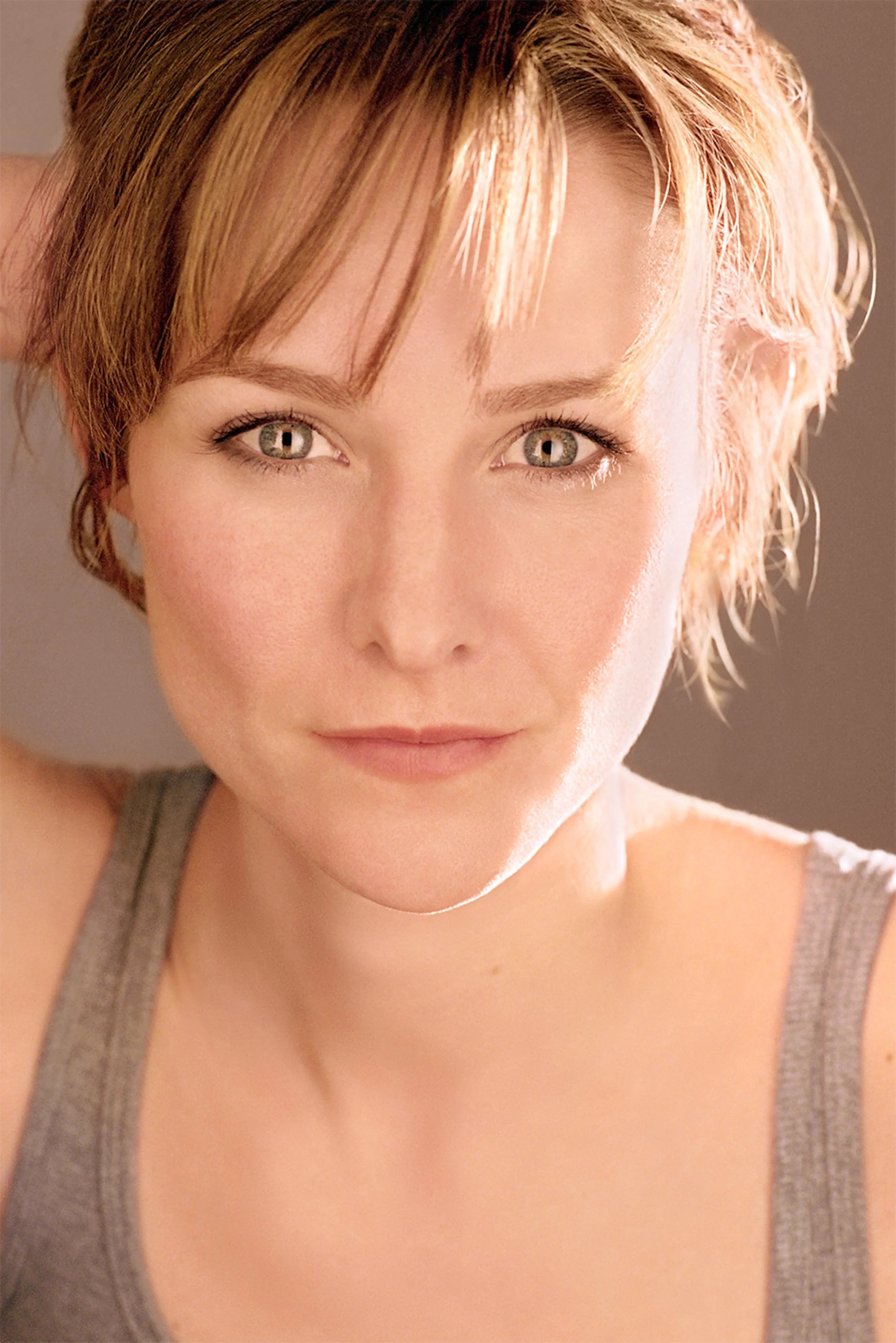 Close-up of a woman with short, reddish hair and hazel eyes, wearing a gray tank top.