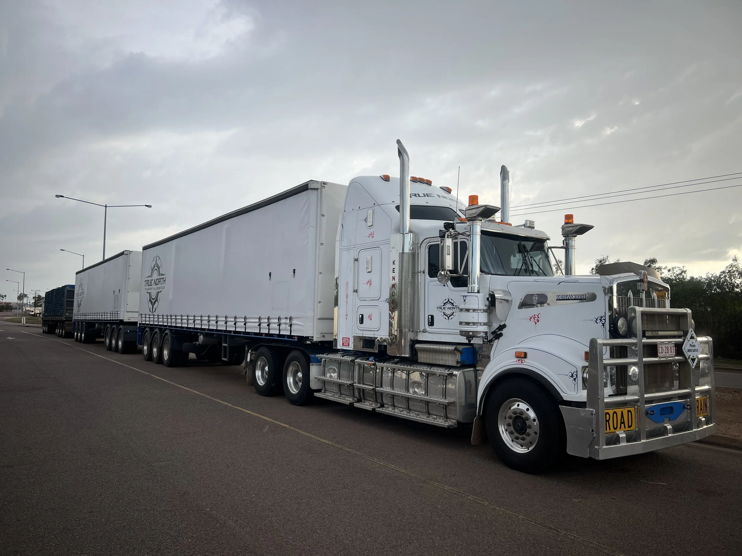Large truck with multiple trailers parked on the side of a road under a cloudy sky.