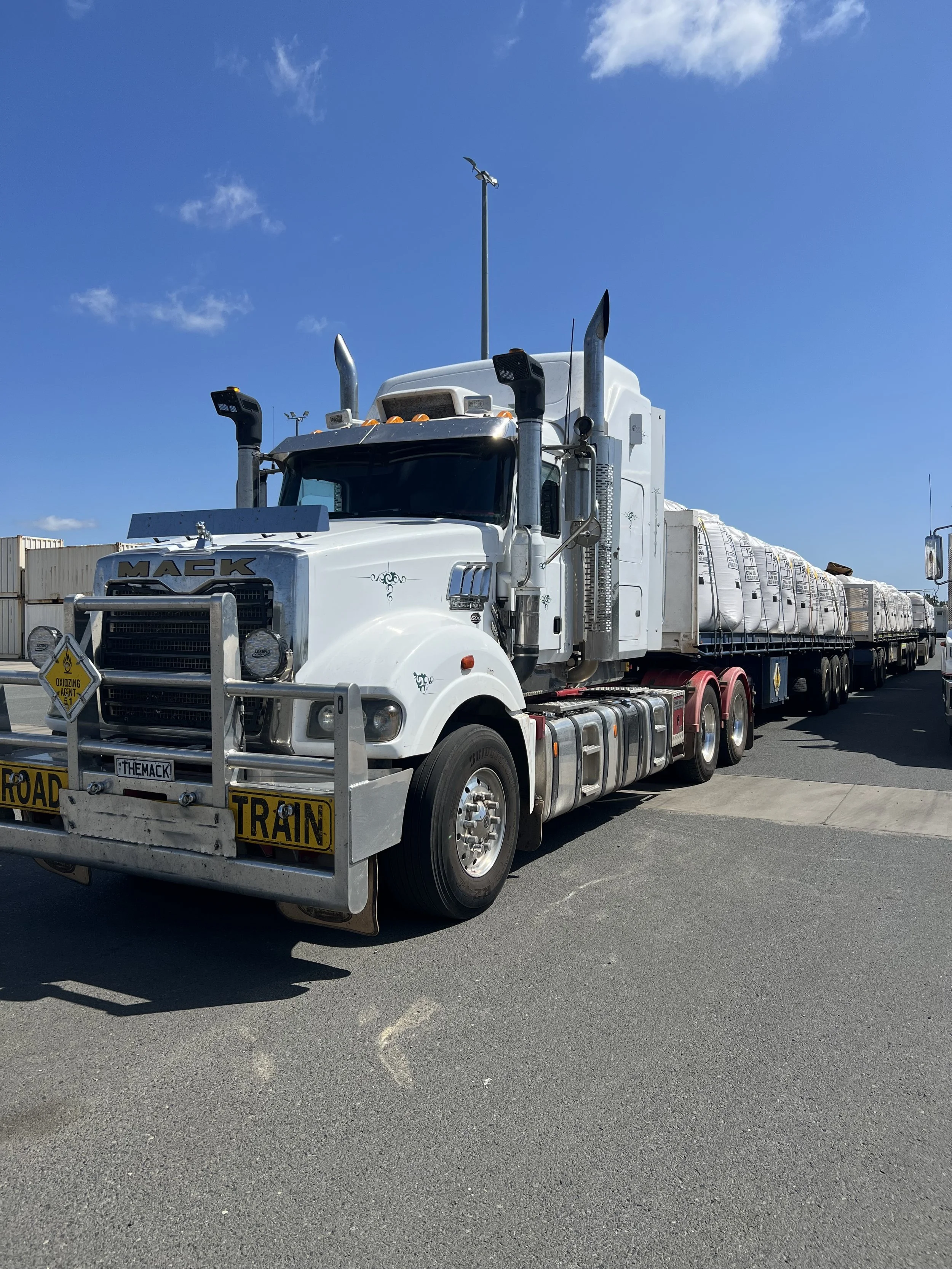 Large white road train truck parked on asphalt, clear blue sky in the background.