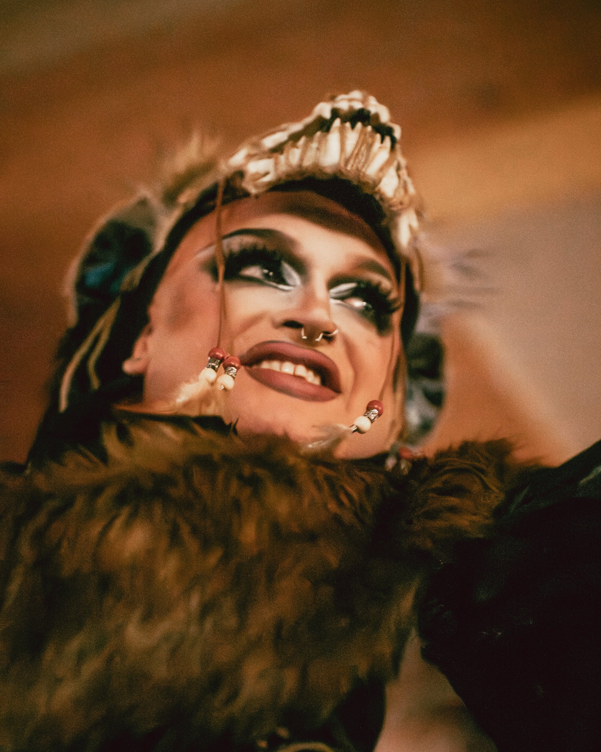 Close-up of a woman with elaborate jewelry, makeup, and clothing, smiling and looking up.