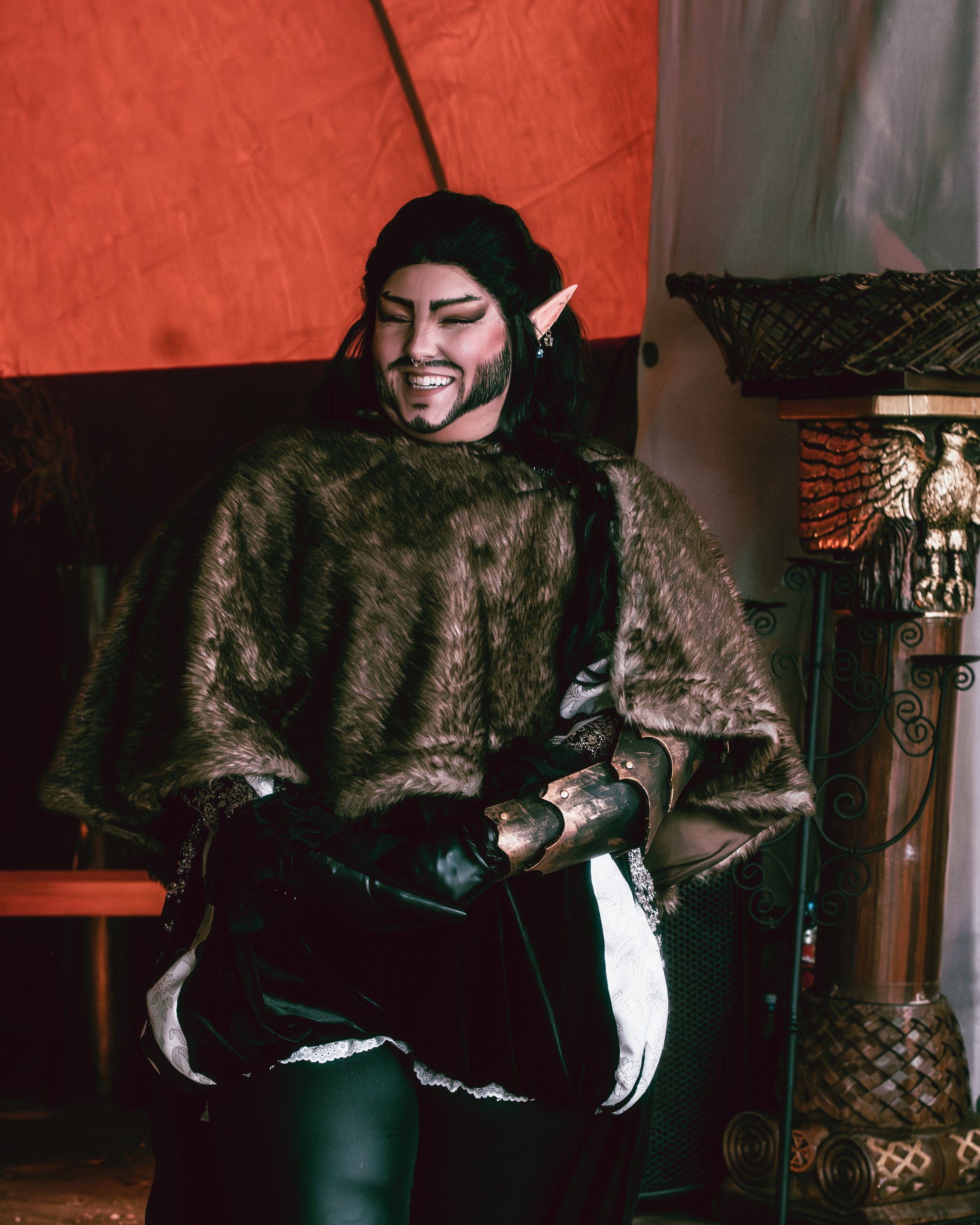Person with elf ears wearing medieval costume, smiling in a dimly lit, fantasy-themed setting.