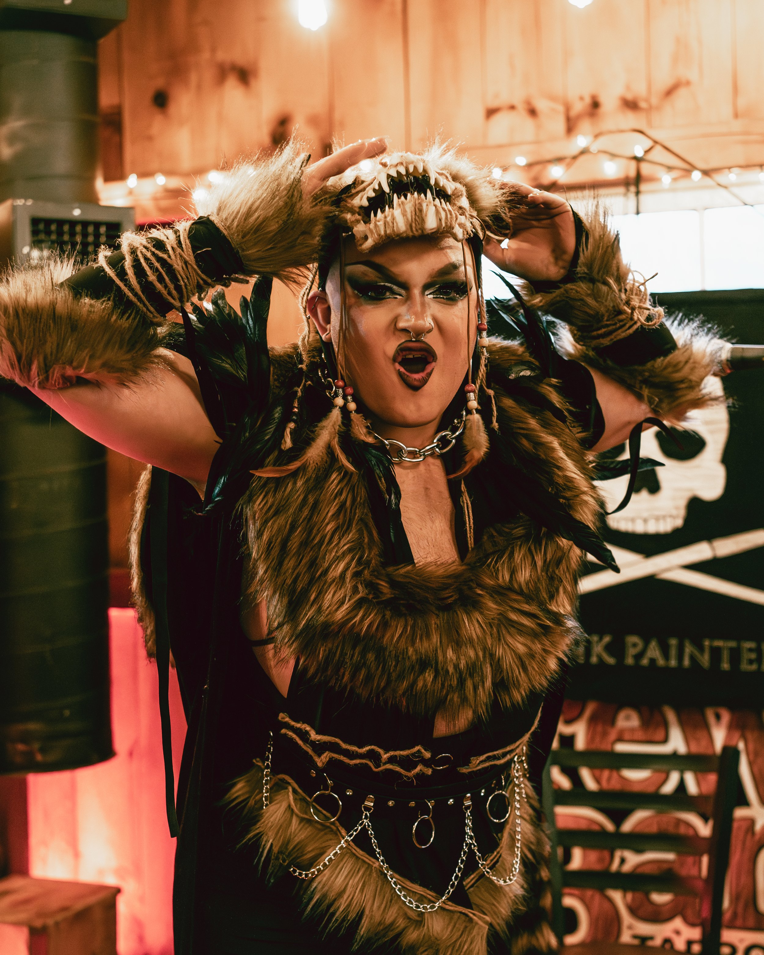 Person dressed in a fierce, tribal-inspired costume with fur and feathers, wearing a skull headpiece and making an expressive face.